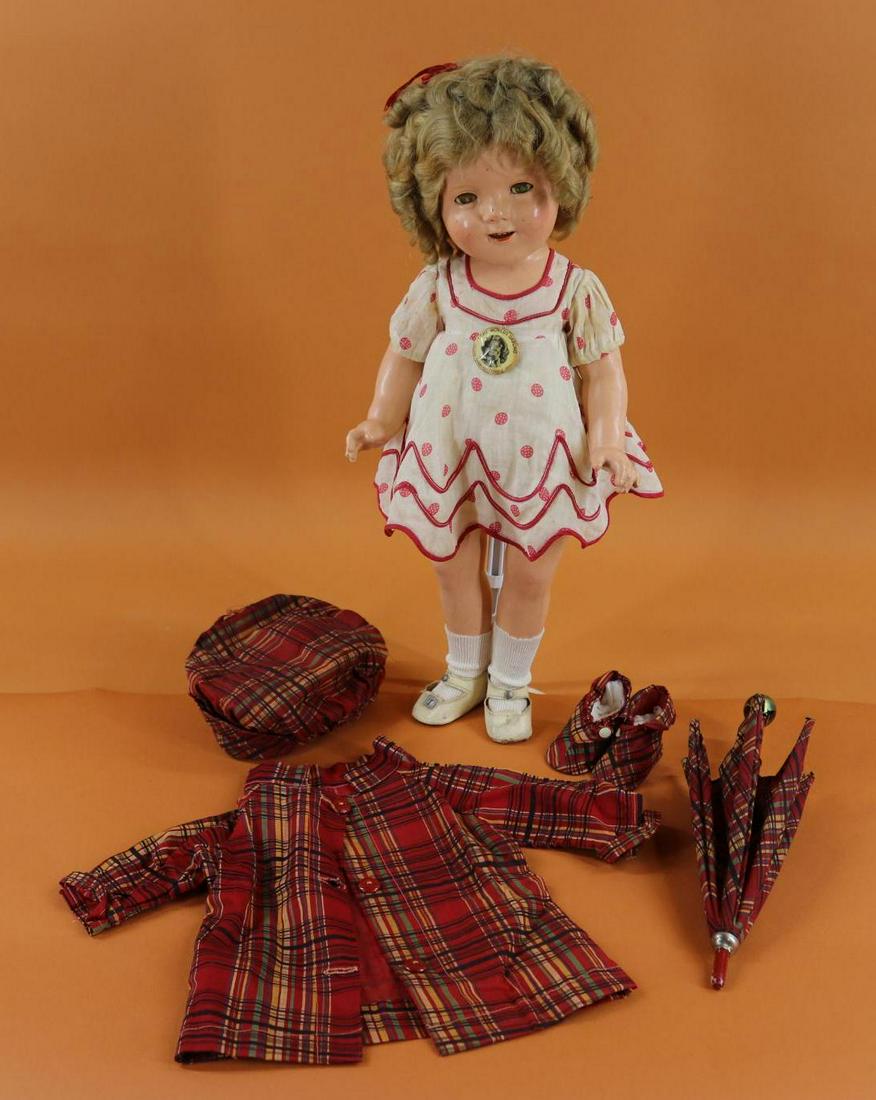 SHIRLEY TEMPLE.: LOT. 19" Ideal composition doll with original mohair wig. Dressed in tagged red/white polka dot dress, oilcloth shoes. Original "The World's Darling" pin. Comes with unmarked red plaid Rain Gear set -