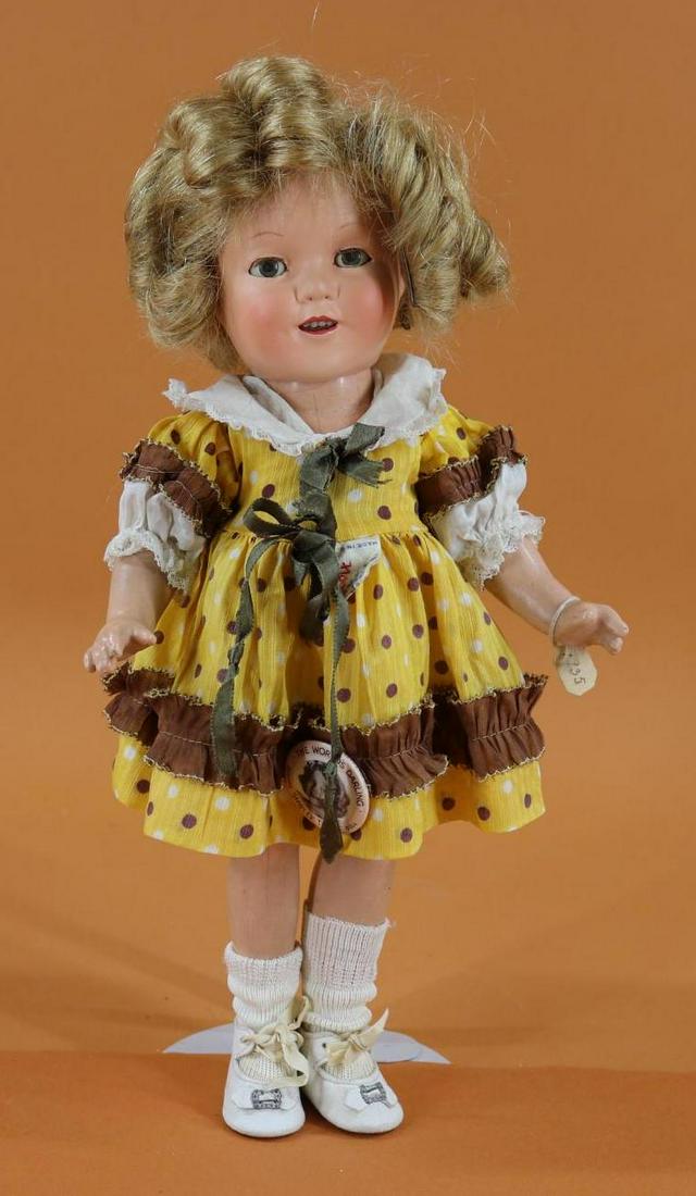 SHIRLEY TEMPLE.: 13" Ideal composition doll with honey blonde human hair wig. Dressed in unusual tagged dimity gold/brown polka dot dress, white leather shoes. Condition: head has had restoration. Some crazing. Eyes a