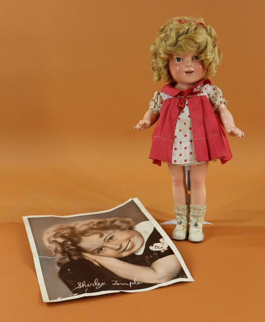 SHIRLEY TEMPLE.: 13" Ideal composition doll with honey blonde mohair wig. Dressed in all original clothing - tagged dress of red dimity and polka dots, 1 pc. undergarment, ivory oilcloth shoes, rayon socks. Comes with