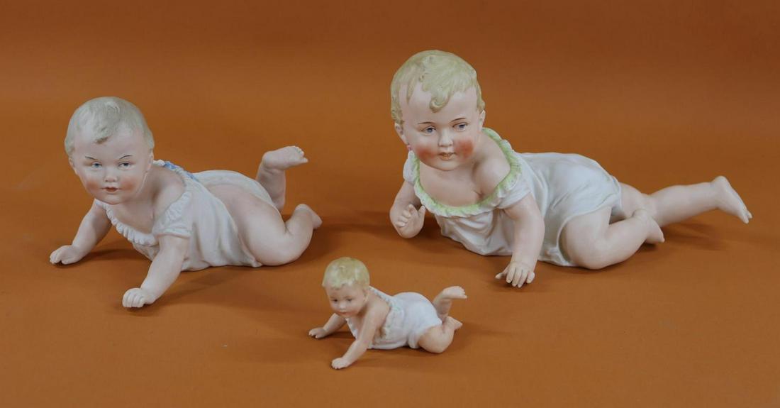 BISQUE FIGURINES.: Lot of (3) German "Crawling Piano Babies" with intaglio eyes. 12" L Baby is marked 436. Condition: fingernail chipped on each hand. The following (2) are marked with the HEUBACH Sunburst. 9" L Baby 31