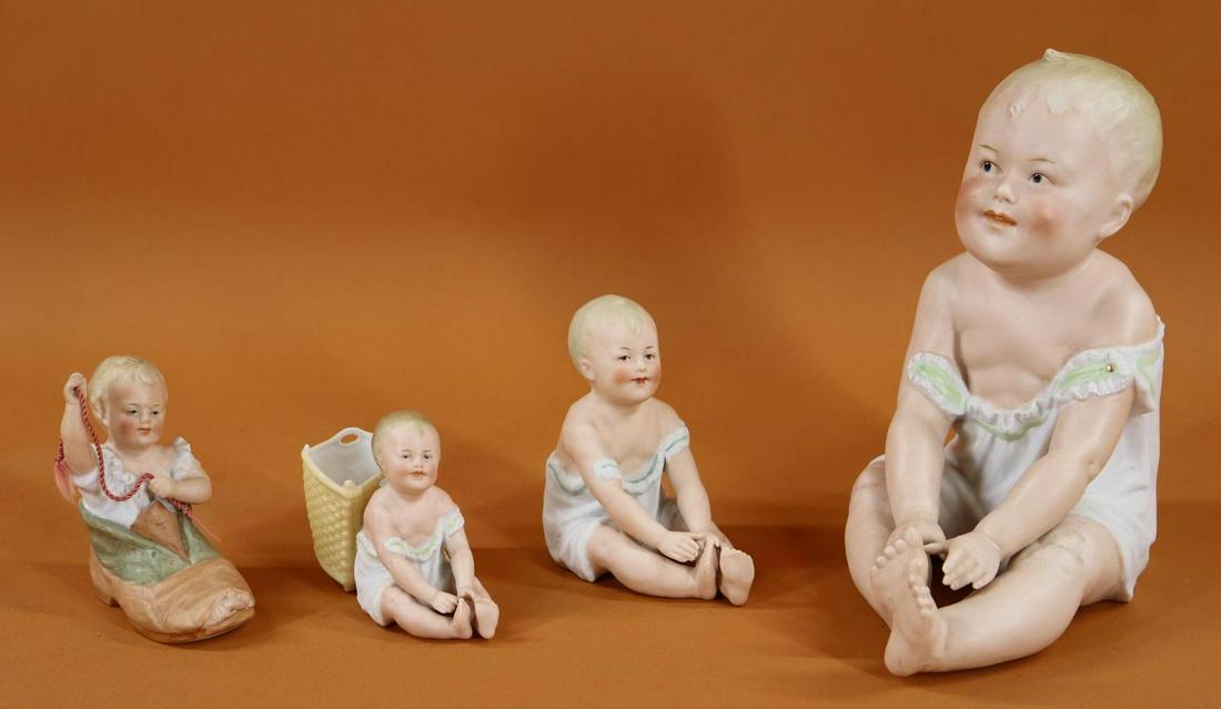BISQUE FIGURINES.: Lot of (4) German "Sitting Piano Babies" with intaglio eyes. 8" Baby marked with the HEUBACH Sunburst. Condition: kiln crack on right wrist (paint touch up) and right ankle; back of clothing. 4 1/4" B