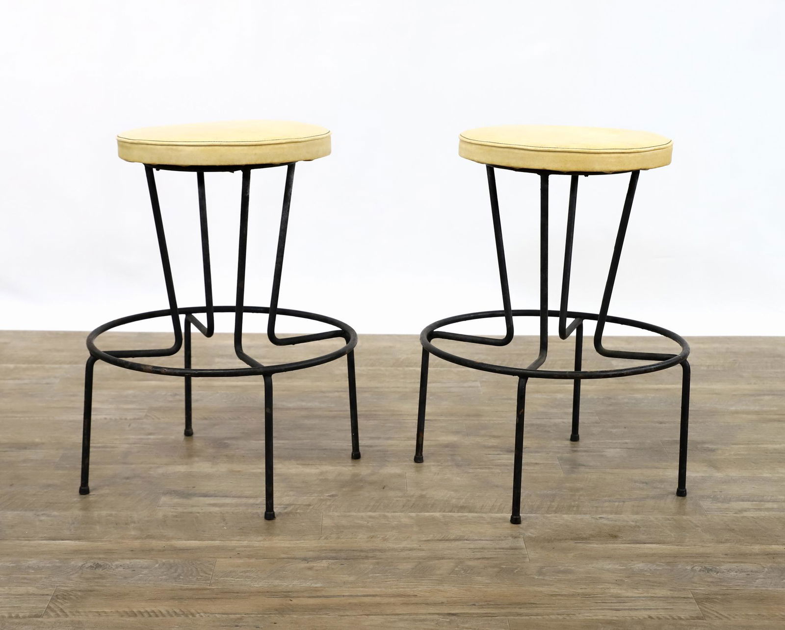 Frederick Weinberg Stools: Cast iron bases with foot rest and beige vinyl upholstery, pair, labeled. 24"h, seat 14"w, base 18.5"w **Please Note: This item is NOT eligible for in-house shipping. Please refer to the terms and con