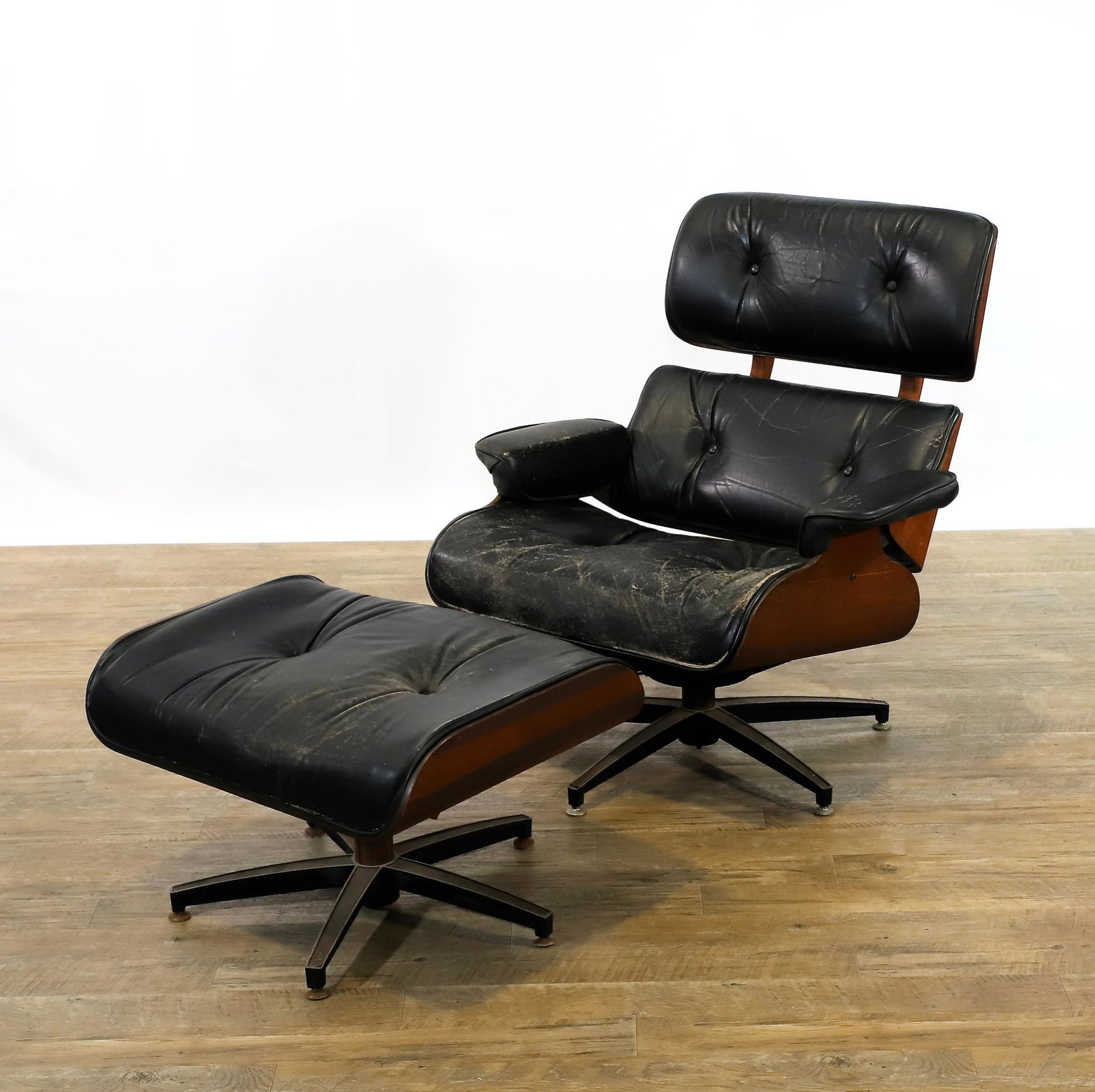 Eames Style Lounge Chair: Mid-century modern lounge chair and ottoman with bent cherry plywood shell and black leather upholstery, manner of Charles and Ray Eames. Wear/alligatoring to the upholstery, and some areas of minor l