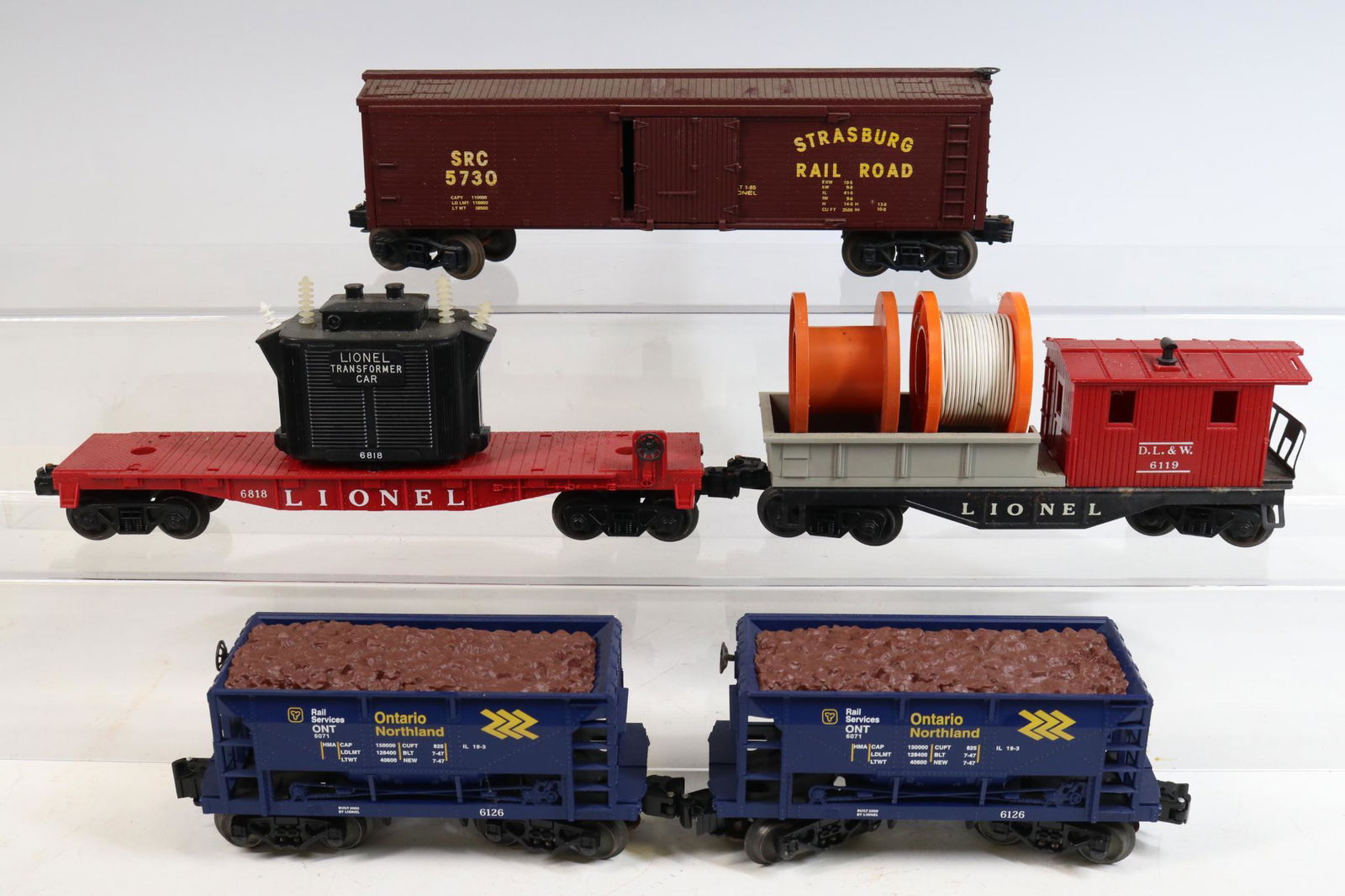 Lionel Train Cars: O gauge train cars including D.L.&W. Working caboose #6119, transformer flatcar #6818, Strasberg boxcar #5730 and (2) Ontario Northland ore cars #6126. â€‹â€‹â€‹â€‹â€‹â€‹