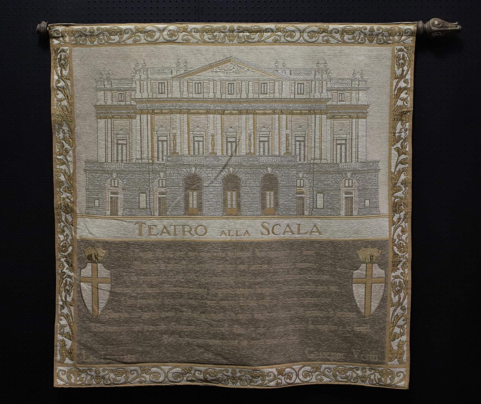Tapestry: Italian tapestry depicting the Teatro all Scala, with writing by Giuseppe Verdi. One end of the rod is broken and missing. 57"h x 57"w, rod 66"