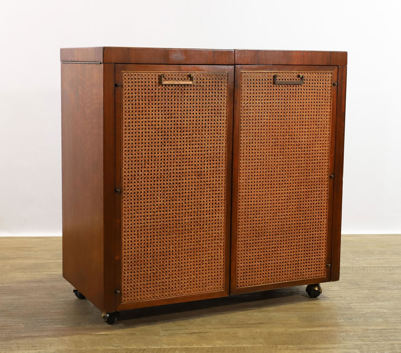 Jack Cartwright for Founders Server: Walnut server / bar on casters, featuring caned doors which open to a drawer and adjustable shelving, and a flip top which opens to a black laminate surface. Labeled. Some minor surface wear. 35.5"h x