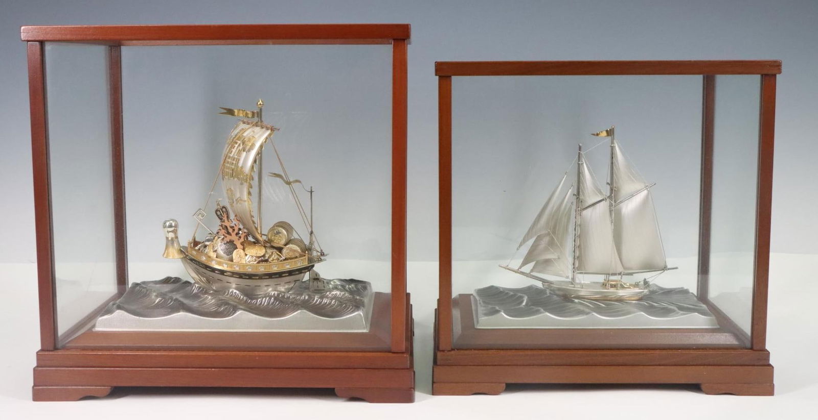 Seki Takehiko Sterling Silver Ships: Japanese 960 silver and gold plated ship models (2), including a junk and a yacht, on silver plate water platforms, mounted to display cases. 10”h x 10.5”w x 7”d