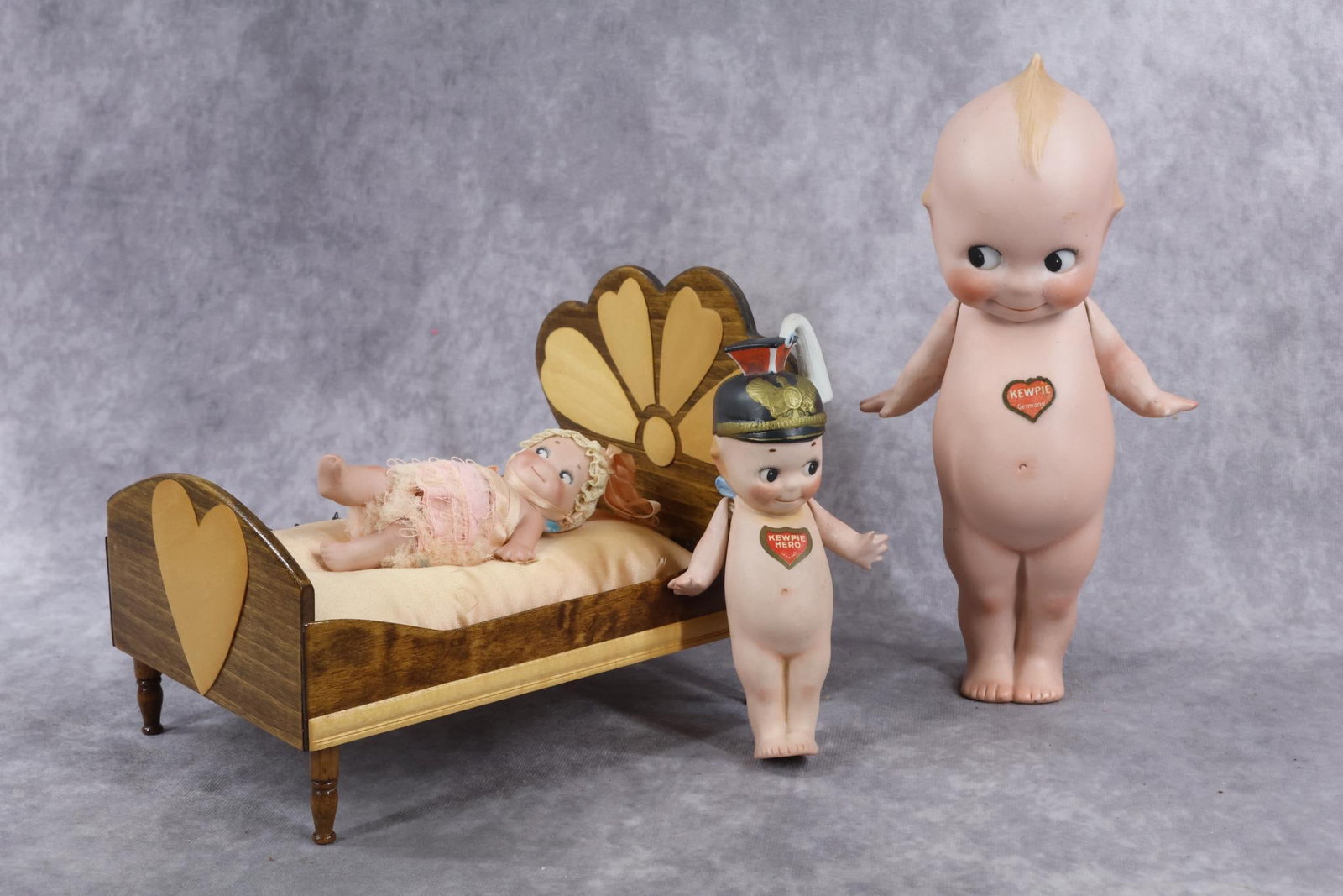 GERMAN ALL BISQUE DOLL(S).: LOT of (4) KEWPIE dolls. 5 3/4" "Kewpie Hero" action Kewpie. Doll has molded hat, paper heart label on front, O'Neill label on back. Strung arms only. 8 1/2" Standing Kewpie with paper heart label on