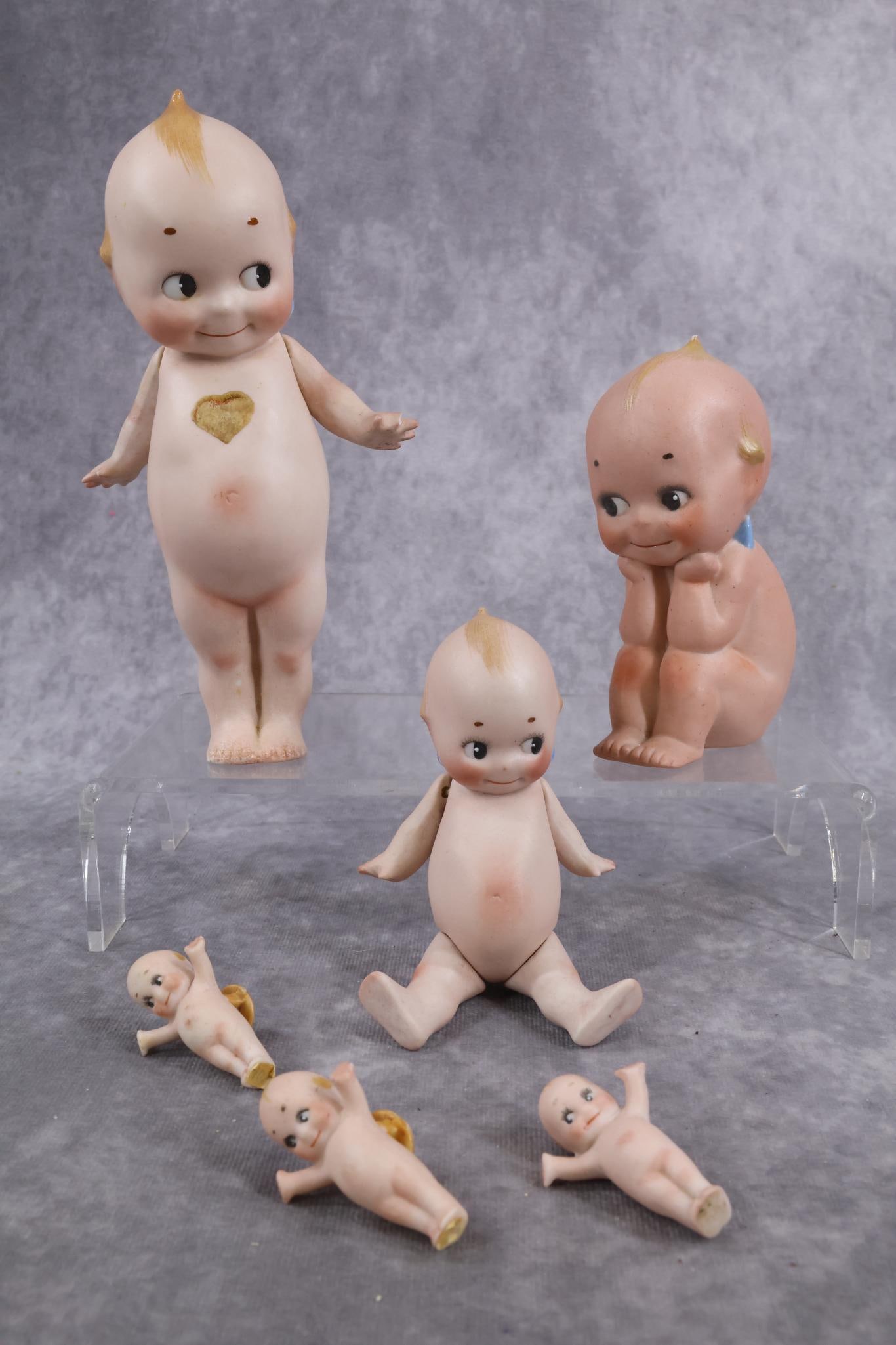 GERMAN ALL BISQUE DOLL(S).: Lot of (6) KEWPIES. 7" Standing Kewpie with paper heart label on front. Marked O'Neill on feet. Strung arms only. (Chipped right wing.) 5" Standing Kewpie with jointed hips. (Flakes on left hip.) 4 1/
