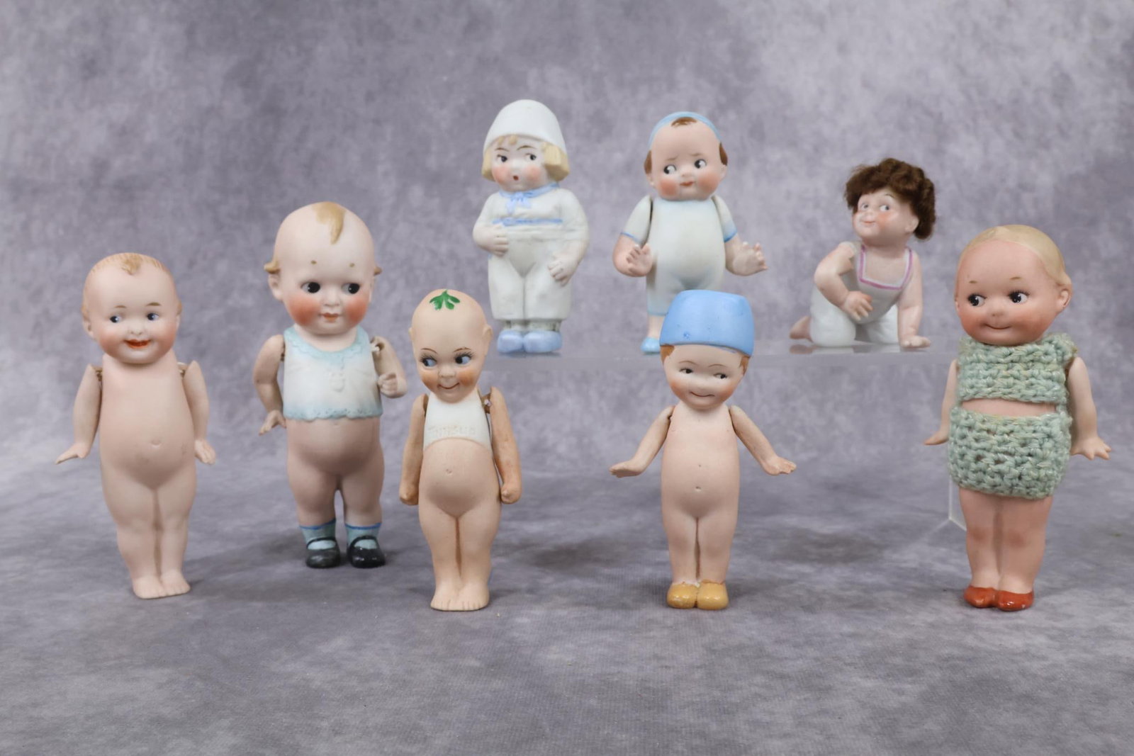 GERMAN ALL BISQUE DOLL(S).: LOT of (8) dolls. (6) Of these have some or all painted clothing. 3 1/2" - 3" Creeping baby with brown mohair wig marked 879-1, (Doll has a repaired right arm.) 5". Dutch immobile. (6) Have strung arm