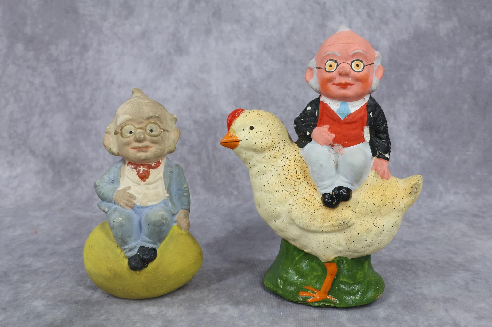 NOVELTIES/HOLIDAY.: NOVELTY - Pair of German "Foxy Grandpa" papier mache Candy Containers. 5 1/2" Foxy Grandpa sitting on an egg. (Bottom piece under egg is missing.) 6 1/2" Foxy Grandpa sitting on the back of a baby chi
