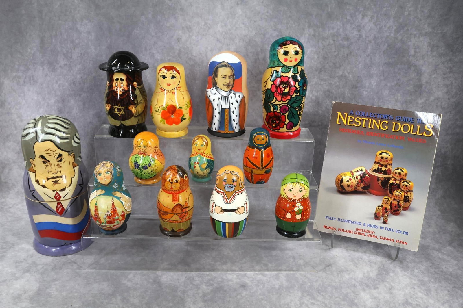 WOODEN DOLL(S).: LOT of (12) Nesting Dolls and book. All of these have been made in the USSR. Some are signed by the artist on bottom. They range in height from 3 1/2" - 11". All have multiple pcs. 3 1/2" Girl with ch