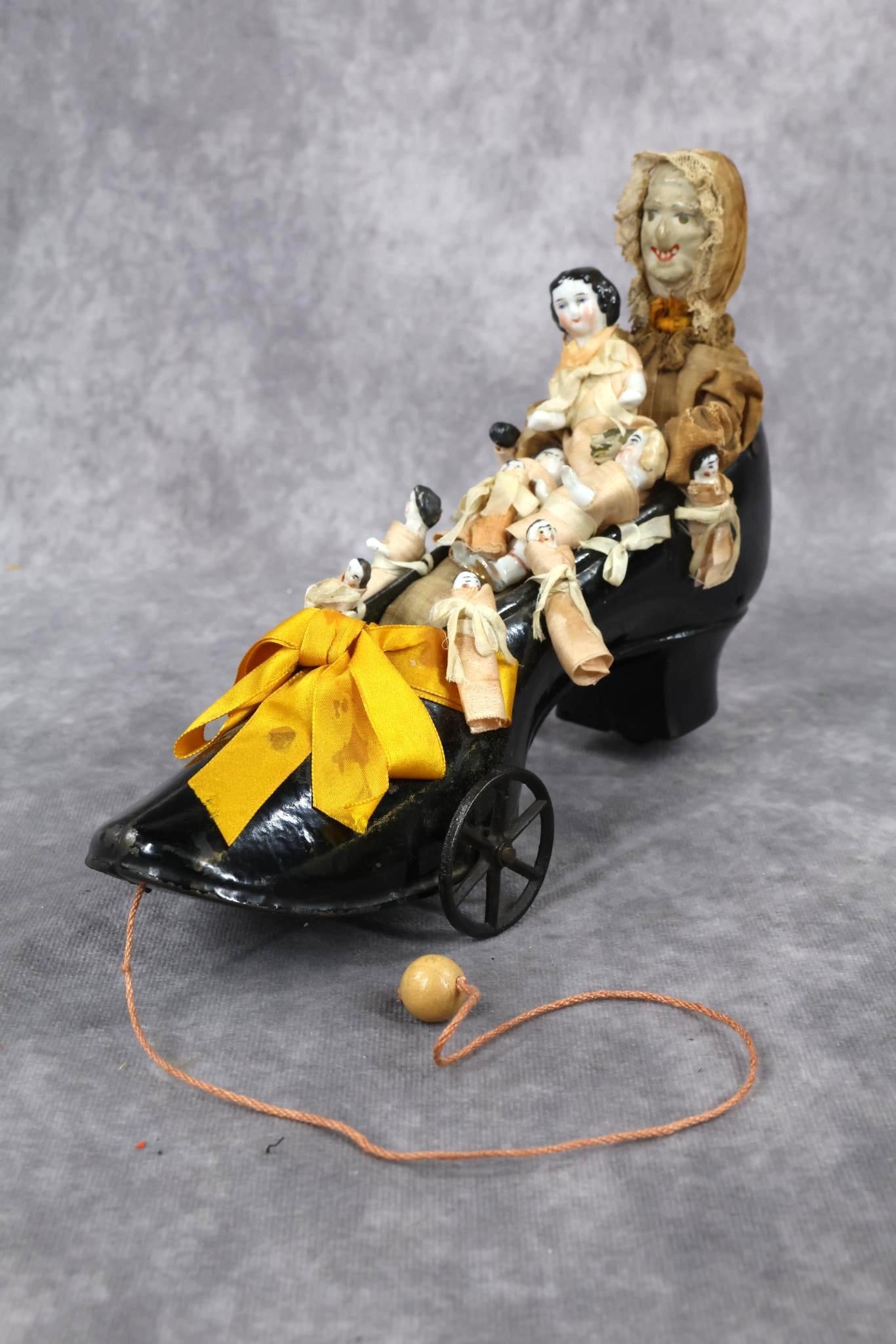 TOYS.: 9" L. Cast iron "Old Woman in a Shoe" pull toy. Shoe is holding the original Old Woman in her original clothing. She comes with (11) china Frozen Charlotte dolls and (1) Parian type with wire strung a