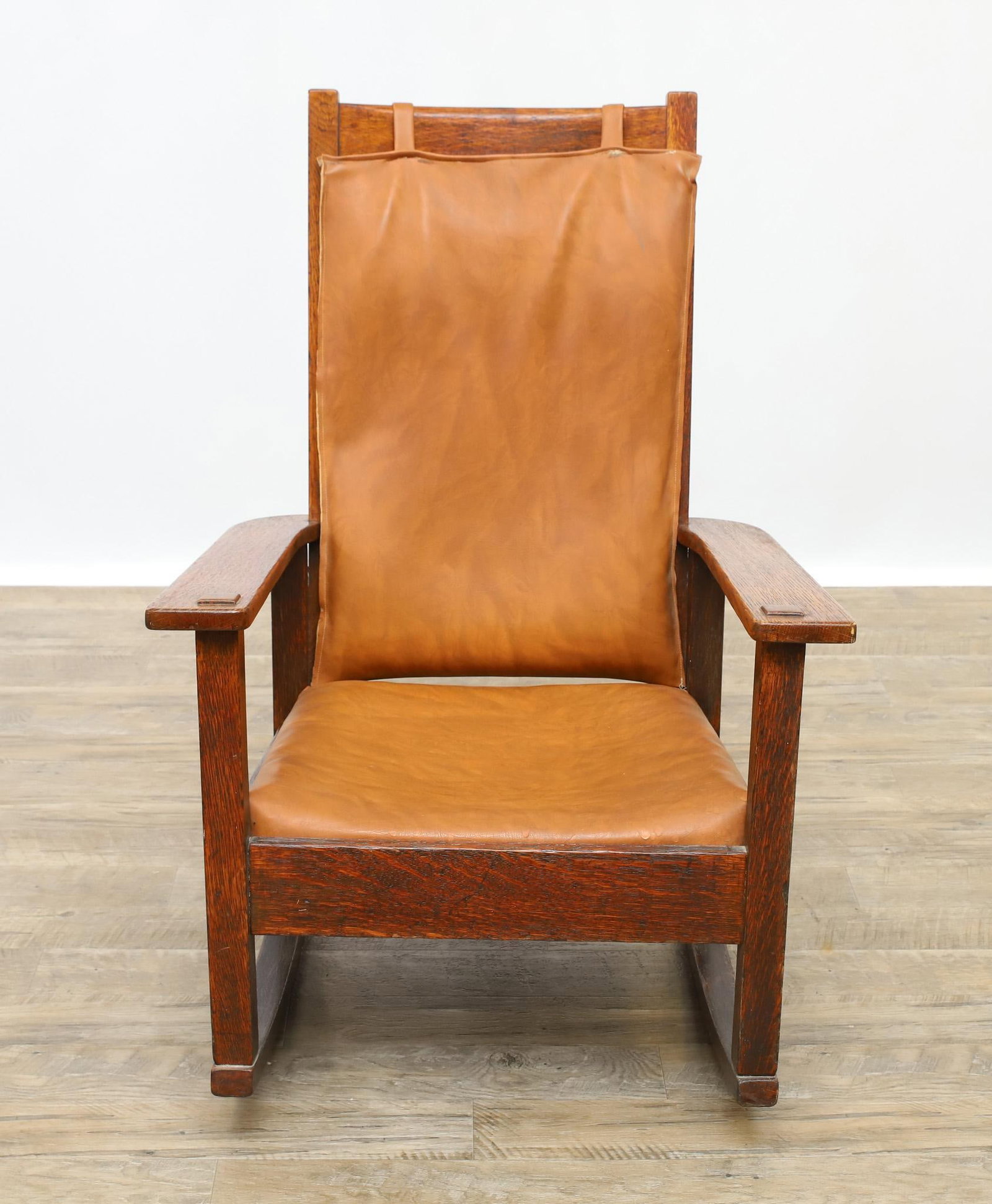 Stickley Brothers Quaint Rocking Chair: Quarter sawn oak Mission rocking armchair with slat back and through tenon construction, with leather seat and back cushions, the back cushion tacked-in. Retains early 20th C. brass label. 40"h x 27"w