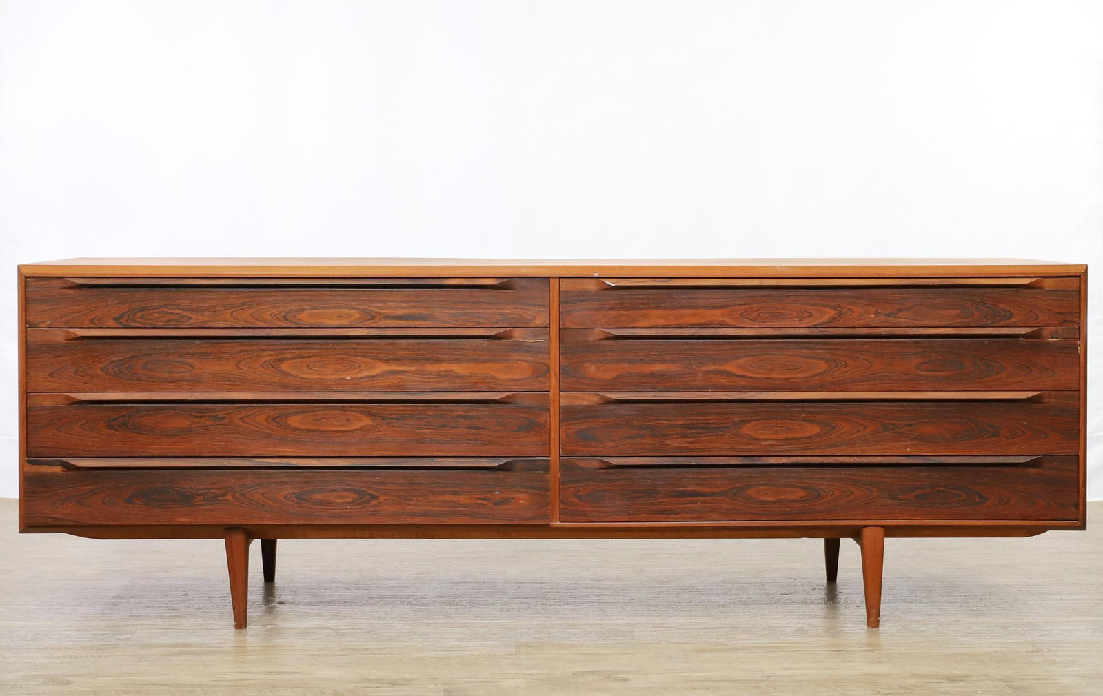 Rosewood and Teak Low Dresser: Manner of Ib Kofod Larsen, a low dresser with a configuration of eight drawers, some fitted, attached to stands with shaped tapered legs. unmarked. One support has extensive repairs. One drawer does n