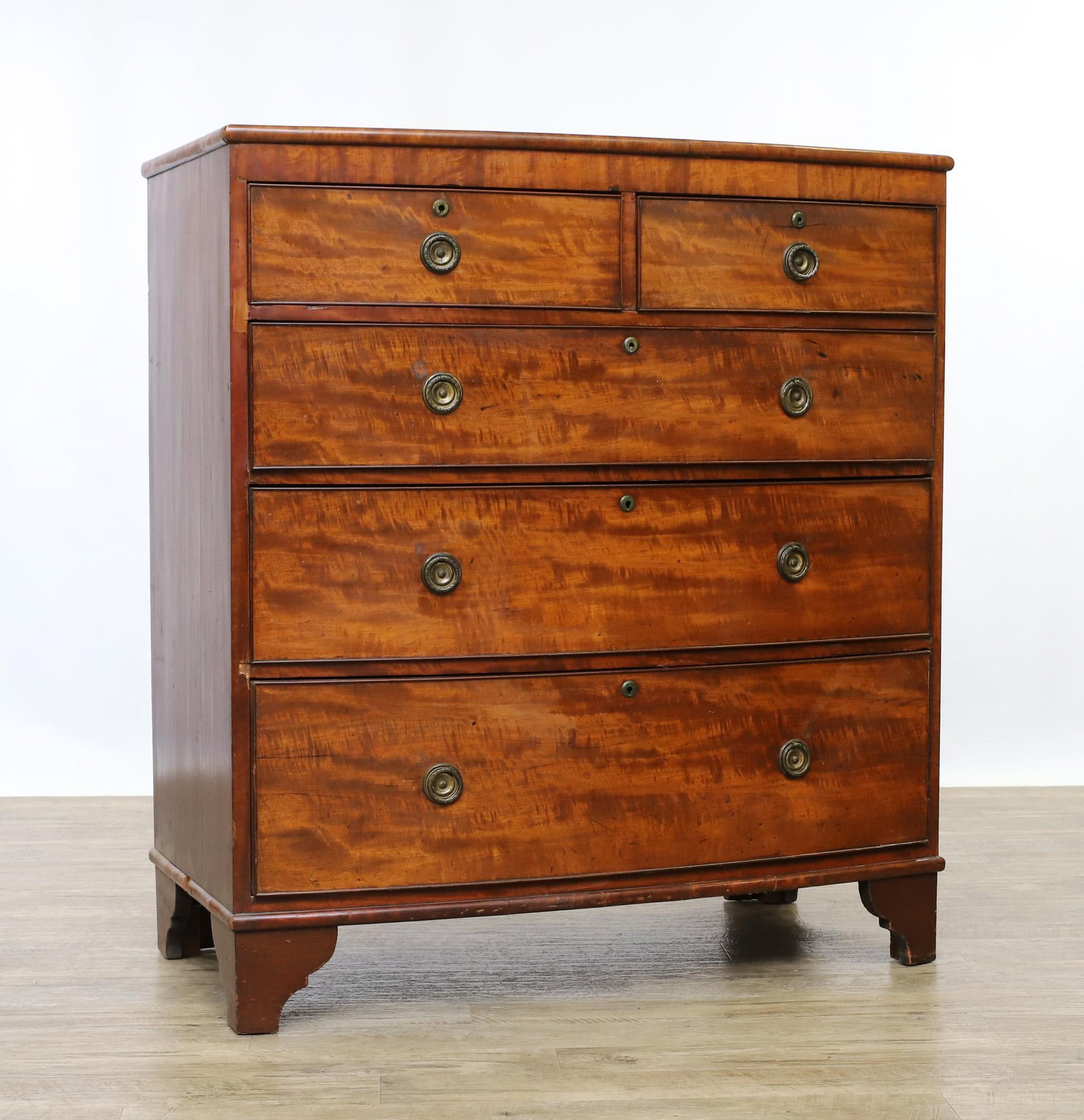 Georgian Bow Front Chest of Drawers: Flamed mahogany case with veneering, two short over three graduated dovetail drawers with oak secondary, on shaped bracket feet. Case exhibits some veneer and molding loss. 44"h x 40"w x 20"d
