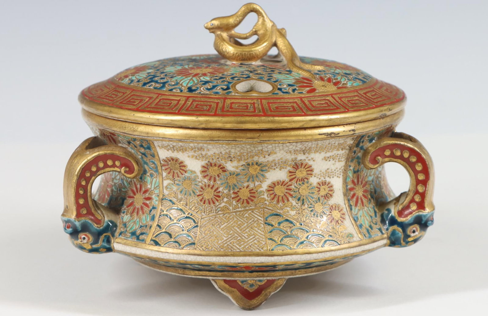 Japanese Satsuma Pottery Censer: Meiji era footed round censer with a tapered body, grotesque mask form handles, snake form finial, and floral decoration with a meander border and gilt accents, unidentified mark, possibly Katei or Mu