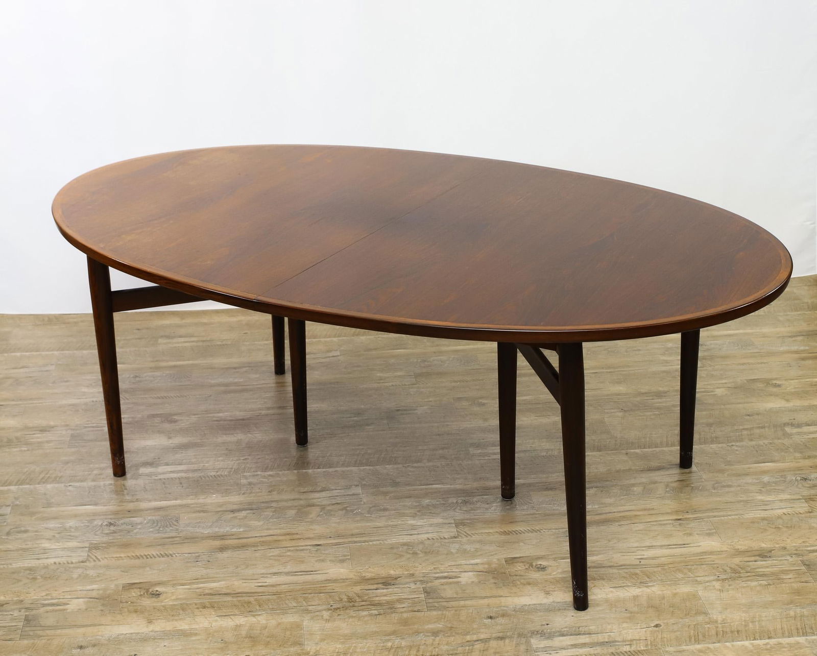 Arne Vodder for Sibast Rosewood Dining Table: Model 212 oval extension dining table with cross banding, on six tapered cigar legs with double stretchers, and two leaves, unmarked. Areas of sun bleaching and other minor surface wear. 28.5"h x 49"d
