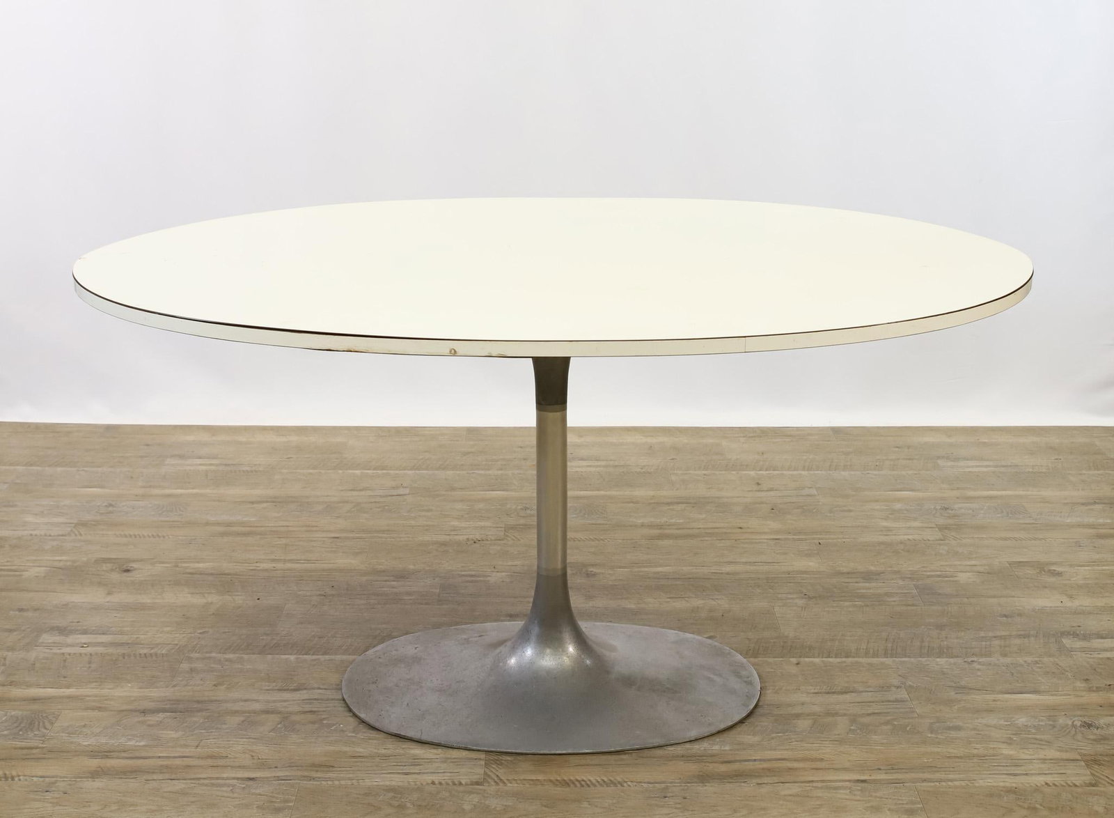 Tulip Dining Table: Oval white laminate top on an aluminum pedestal base. Areas of laminate exhibit separation form table. 29.5"h x 58"w x 39.5"