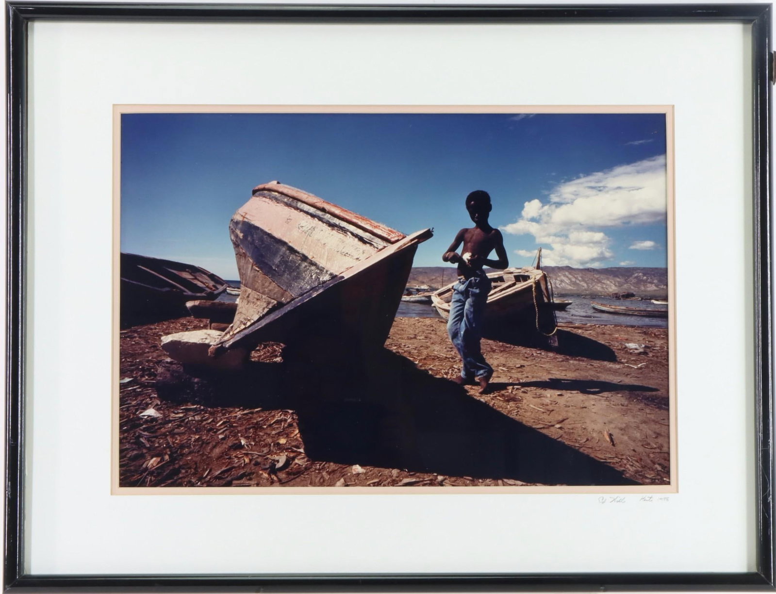 Ed Hille (20th c): Photograph, "Haiti" 1988. SLR to matte. Portrait of a young boy near a fishing boat. 12.5"h x 18.5"w and 20"h x 26"w