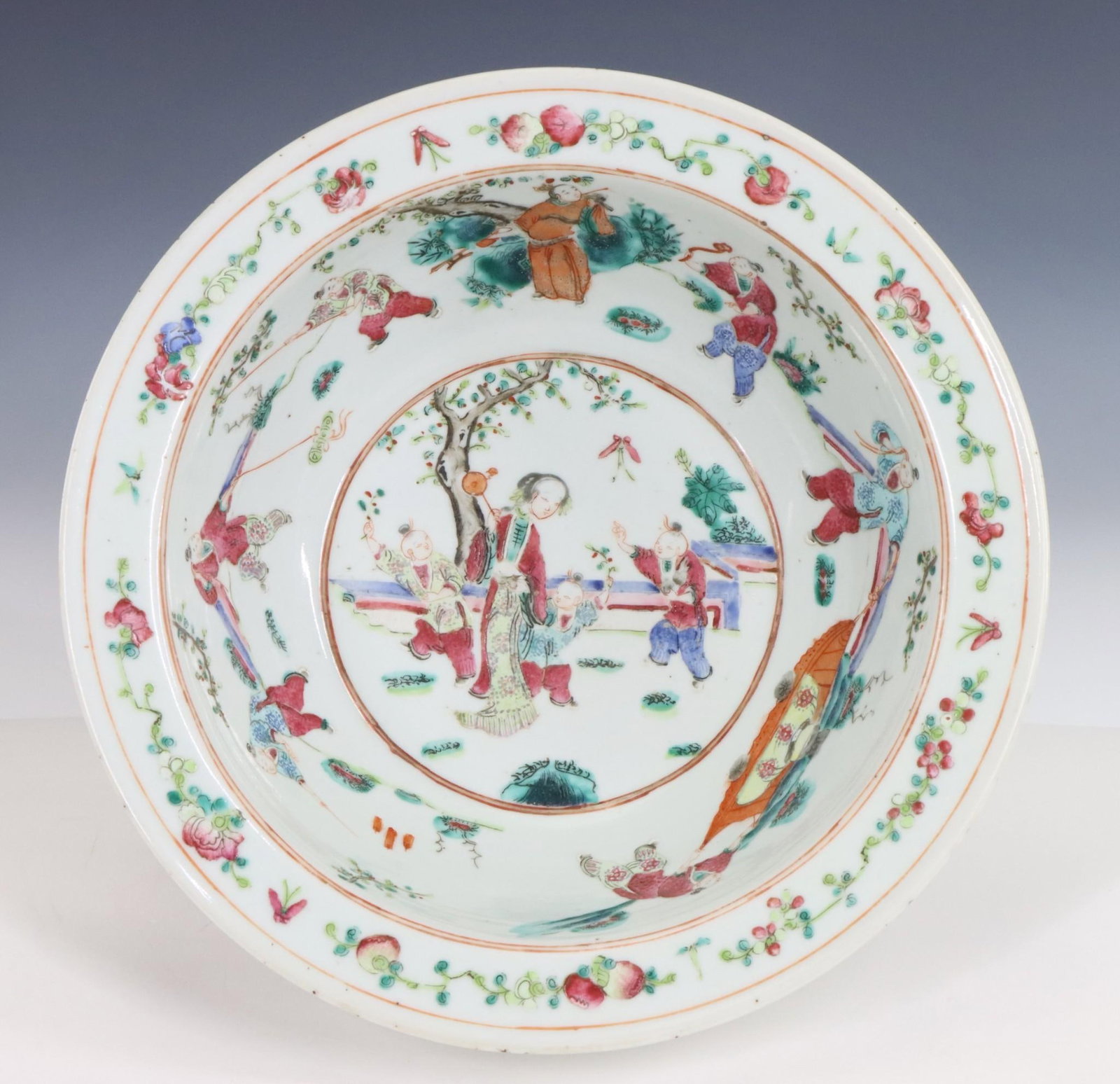 Chinese Famille Rose Bowl: Qing era serving bowl decorated with boys playing in a garden with a female attendant, the rim decorated with peaches, flowers, and butterflies, and the exterior with iron red foliage. 3.75"h x 11.5"w