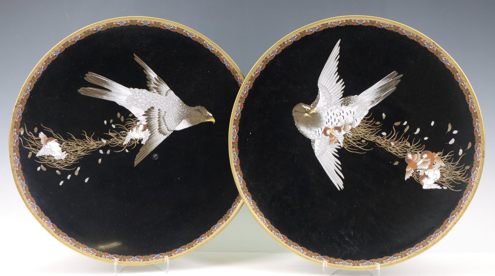 Japanese Cloisonne Chargers: Meiji - Taisho era pair of cloisonne chargers depicting hawks attacking young sparrows against a black ground with polychrome stylized foliate borders, the underside of the rims decorated with wire sc