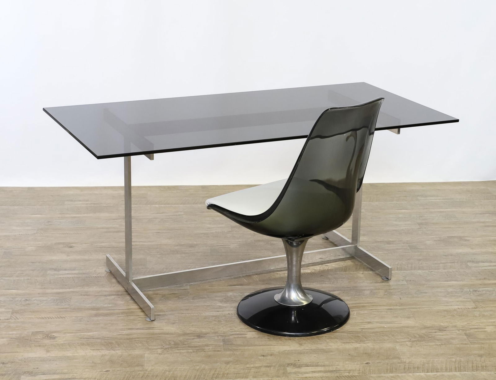 Chromcraft Lucite Chair With Smoke Glass and Chrome Table: Smoke lucite swivel tulip chair with white leather seat and aluminum support, by Chromcraft, labeled. 35.5"h x 20.5"w x 15"d, seat height 17". Smoke glass top table or desk with a chrome steel flat ba