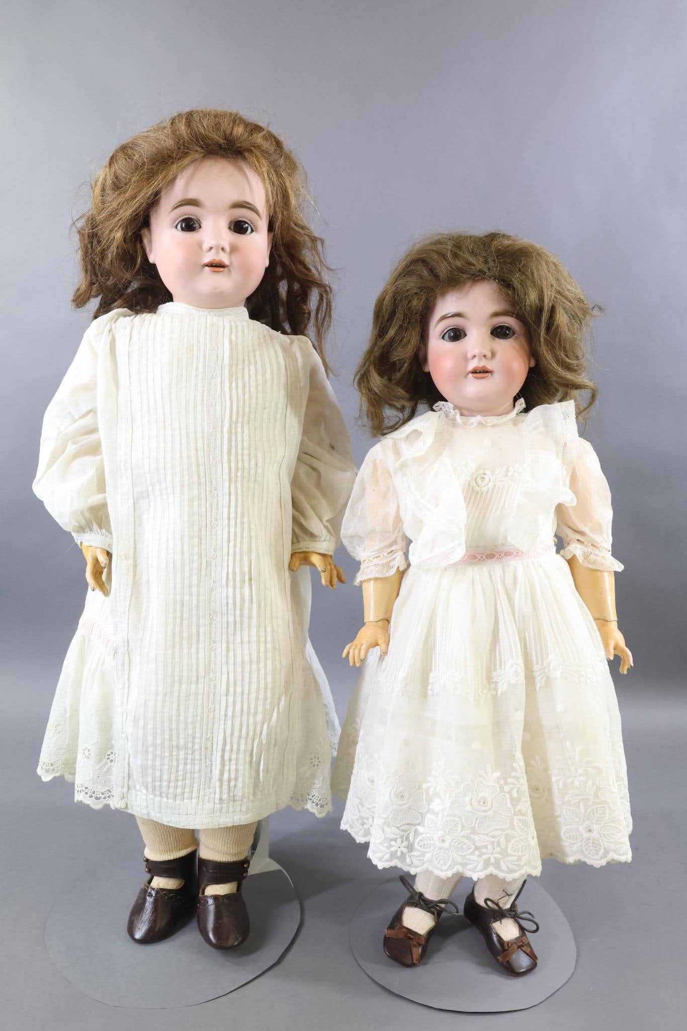 GERMAN BISQUE DOLLS.: Pair of KESTNER 164 dolls. Both dolls have brown sleep eyes, open mouths, brown HH wigs, papier mache ball jointed bodies. Both dolls are dressed in antique white cotton dresses, newer brown leather s