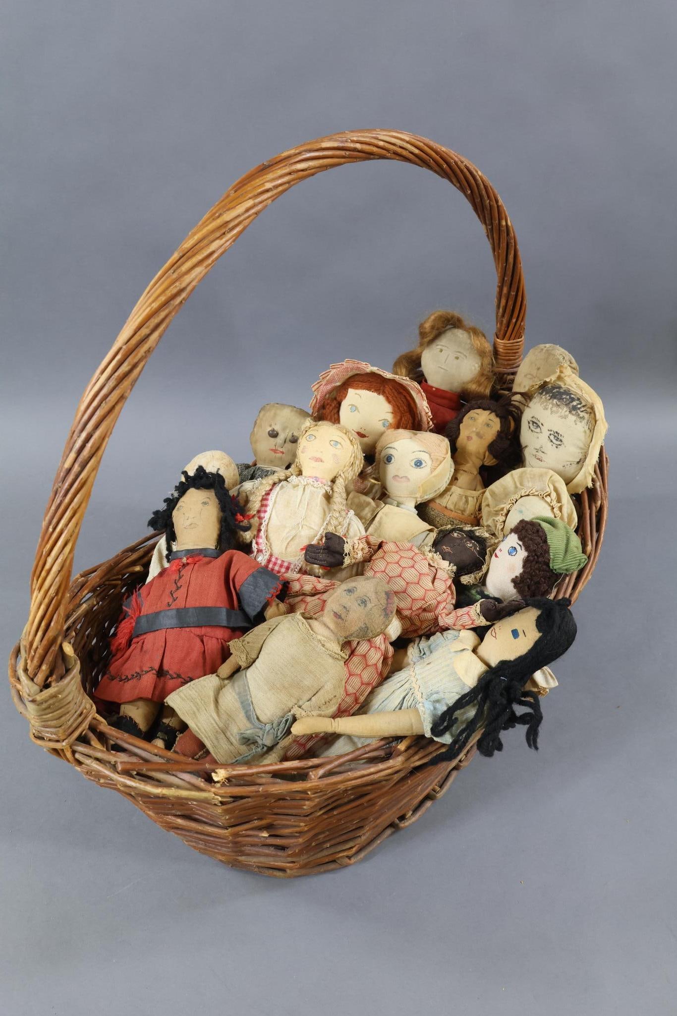CLOTH DOLLS.: LOT of (15) cloth dolls in a large handled basket. This came in from the consignor as she stored them. 7" - 15" Dolls with embroidered faces, painted faces, drawn on faces, printed faces. Hair that is