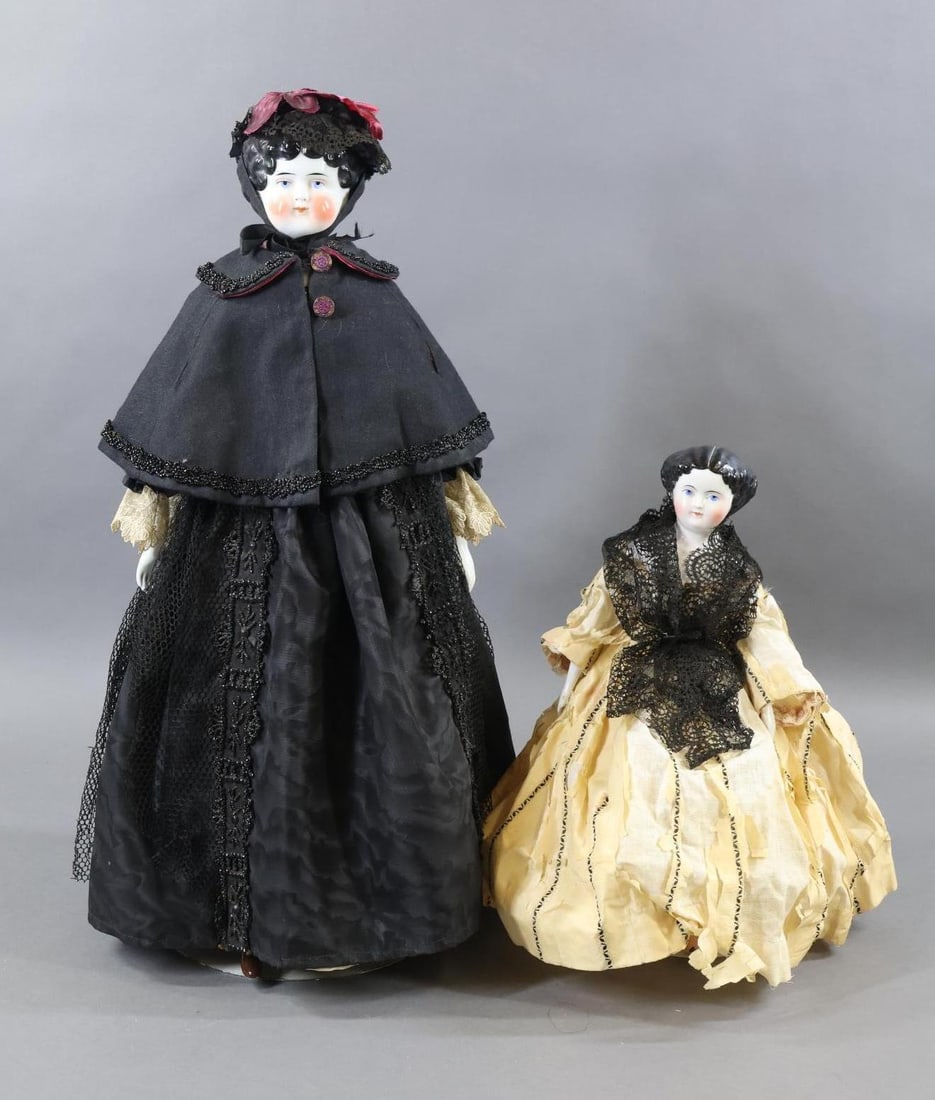 CHINA, PARIAN DOLLS.: Pair of China shoulder head dolls. Both dolls have black center part hair, painted blue eyes. They are both dressed in antique clothing. Doll 1) 14" is an antique head with an 1870's hair style. It is