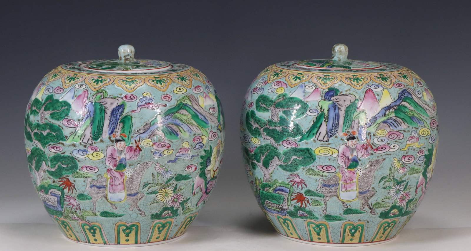 Chinese Famille Rose Jars: Republic era Chinese famille rose porcelain pair of jars with a landscape scene with immortals, qilin, and swirling clouds against a light celadon ground. The covers have rounded finials, and the rims
