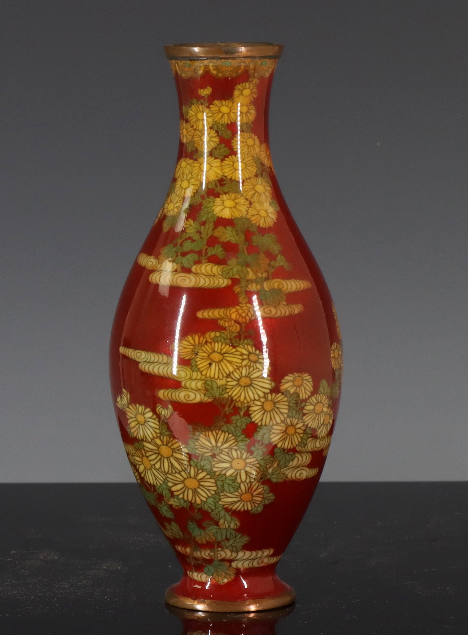 Japanese Cloisonne Vase: Meiji - Showa era cloisonne vase depicting chrysanthemums and stylized cloud motifs on a red ground. Unmarked. 7.5"h x 3"w