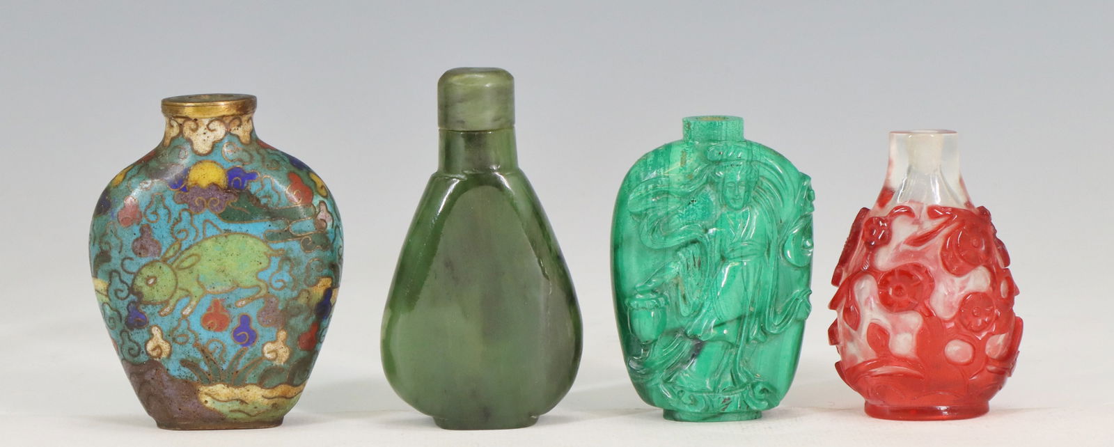 Chinese Snuff Bottles: (4) Chinese snuff bottles including a cloisonné enameled bottle with rabbit motif, a mottle green nephrite jade bottle, a carved malachite bottle with figural design, and a red glass overlay bottle w