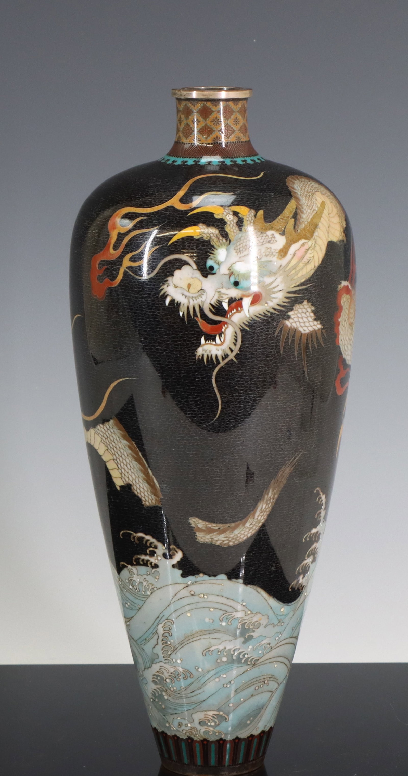 Namikawa Yasuyuki Japanese Cloisonne Vase: Meiji - Taisho era silver wire cloisonne baluster vase decorated with a three-toed dragon in flight over waves on a black ground with wind motif, featuring a false gadroon lower border and an upper bo