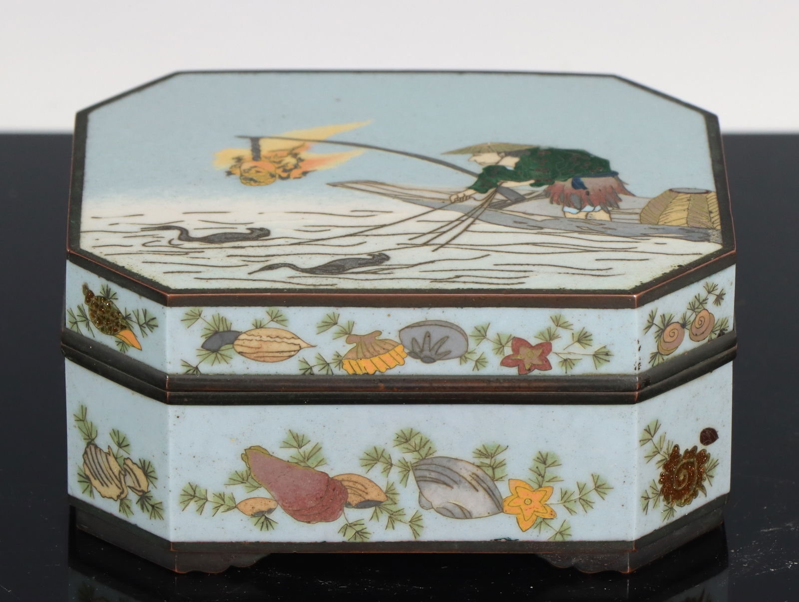 Japanese Cloisonne Box: Meiji - Taisho era silver wire cloisonne hexagonal box with goldstone accents, copper mounts, and bracket feet, the top depicting a scene of cormorant fishing at night, the sides decorated with variou