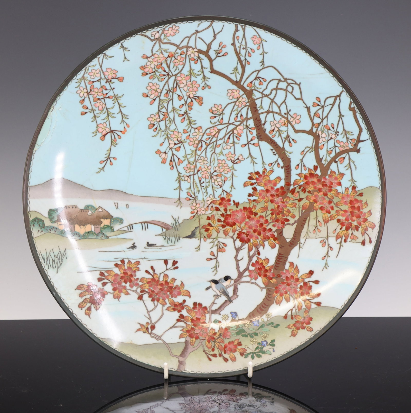 Japanese Cloisonne Charger: Meiji - Taisho era silver wire cloisonne charger decorated with bluebirds among cherry blossoms with a riverside village and mountains in the background, the underside decorated with wire scrolls on a