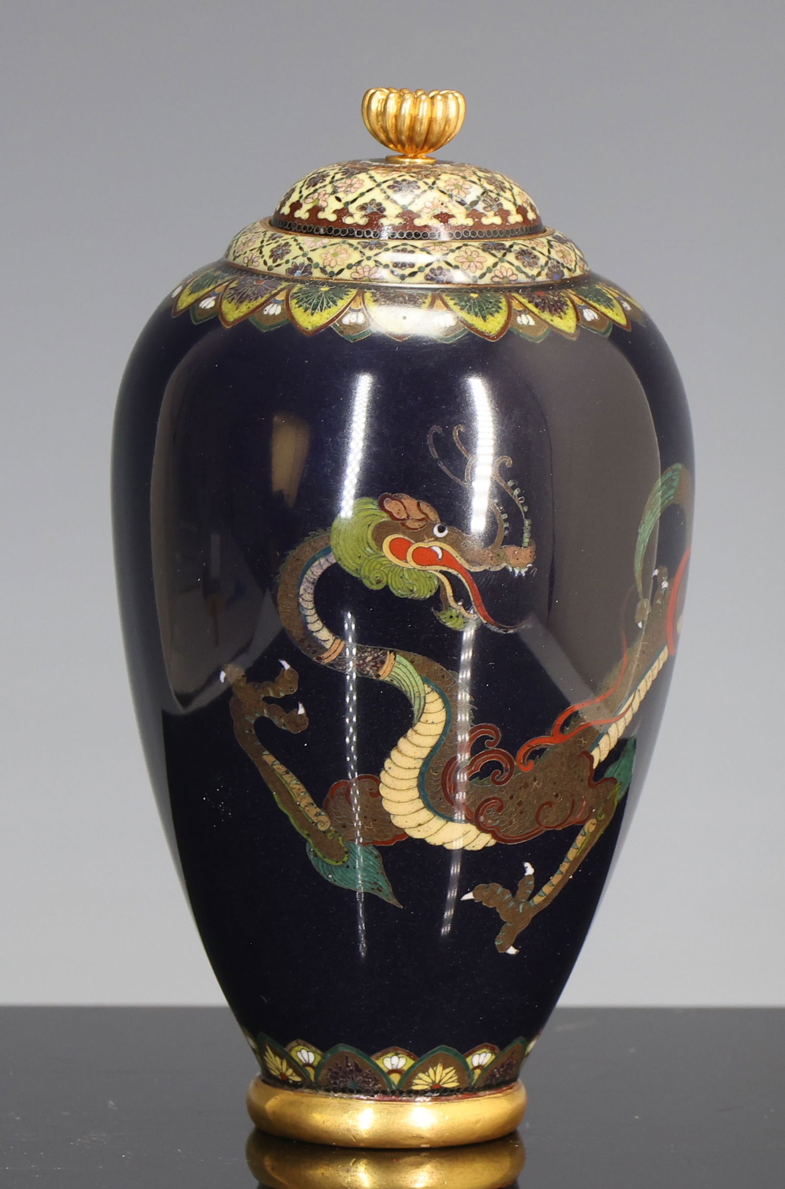 Namikawa Yasuyuki Japanese Cloisonne Urn: Meiji - Taisho era small silver wire cloisonne urn with gilt copper mounts, decorated with a dragon in flight on a black ground, with upper and lower scale and flower borders, the stepped top and dome
