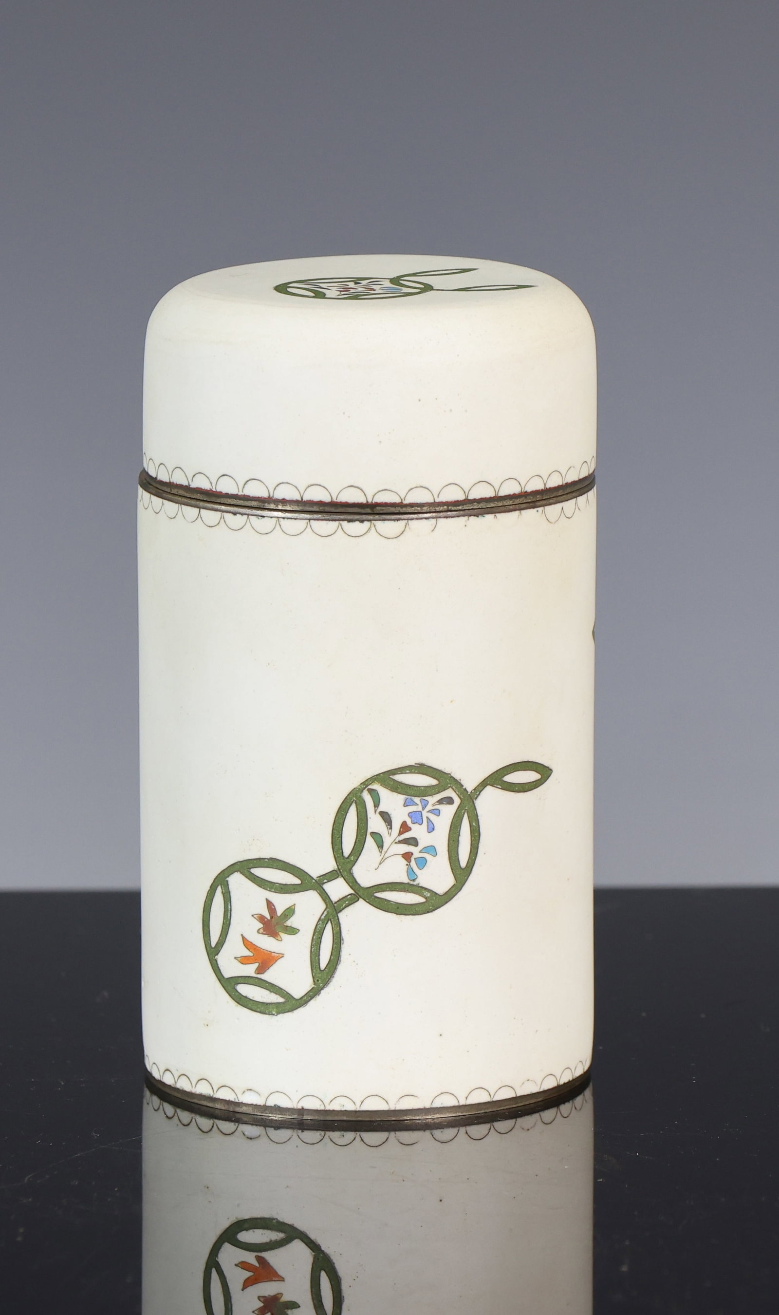 Inaba Japanese Cloisonne Tea Caddy: Showa era silver cloisonne tea caddy with silver plate mounts, cylindrical form with a flower and coin motif on a white ground with a matte finish. Marked Inaba to the foot. 4"h x 2.25"w