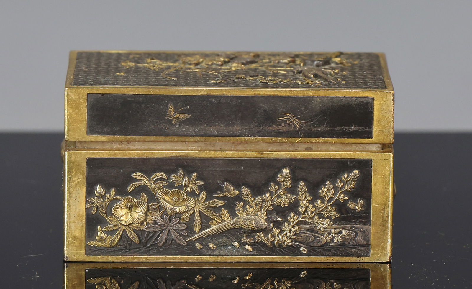Japanese Inlaid Shakudo Stamp Box: Meiji - Taisho era parcel-gilt shakudo stamp box, with takazogan raised inlaid silver and copper decoration depicting birds, butterflies, and flowers, the top with a basketweave relief ground, the int