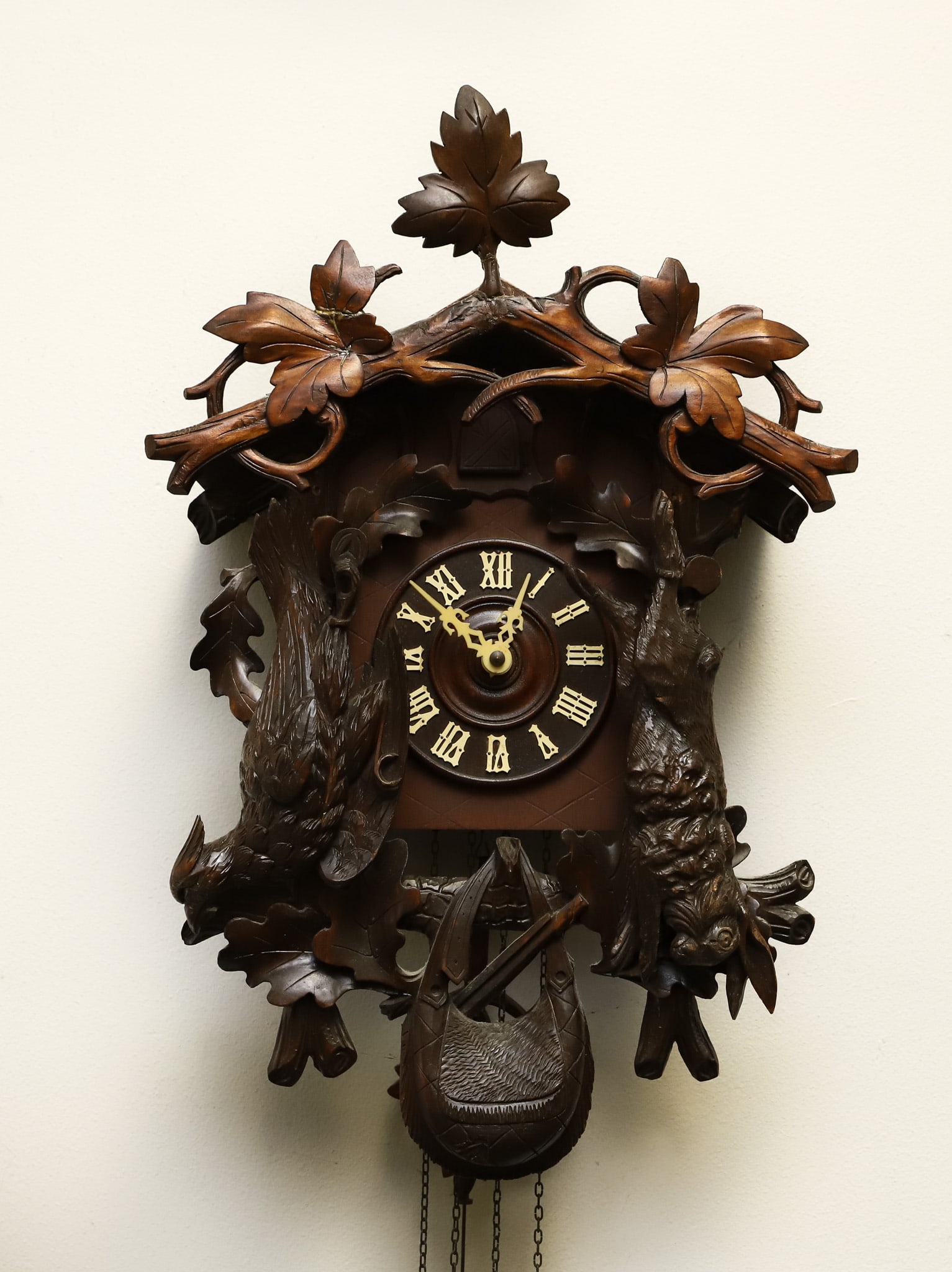 Black Forest Style Cuckoo Clock: Made by the American Cuckoo Clock Co., Philadelphia, PA. Hand carved walnut hunting chalet form case decorated with grouse and rabbit game, hunter's satchel, and foliate and leaf motifs. Pine cone stl