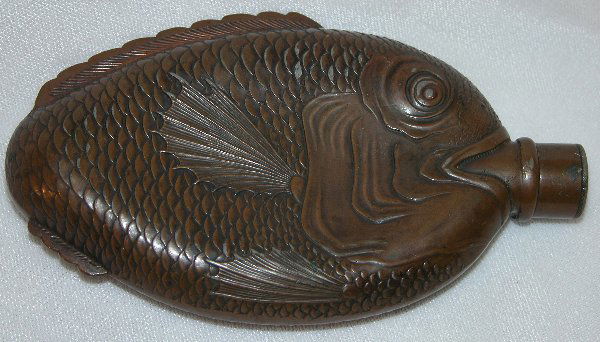 Metal Flask – Fish Form.: Oval form metal flask in fish design, decorated to depict eyes, mouth, fins and scales, tail wraps around to obverse side, neck of flask in fish's mouth, screw-on cap, thought to be late 19th Century,