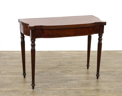 Sheraton Mahogany Card Table: Mahogany Sheraton card table, with a fold over top featuring a rounded front and rear, and turret corners. Reeded, tapered legs ending in turned spade feet. The hinged top folds open to reveal a polis