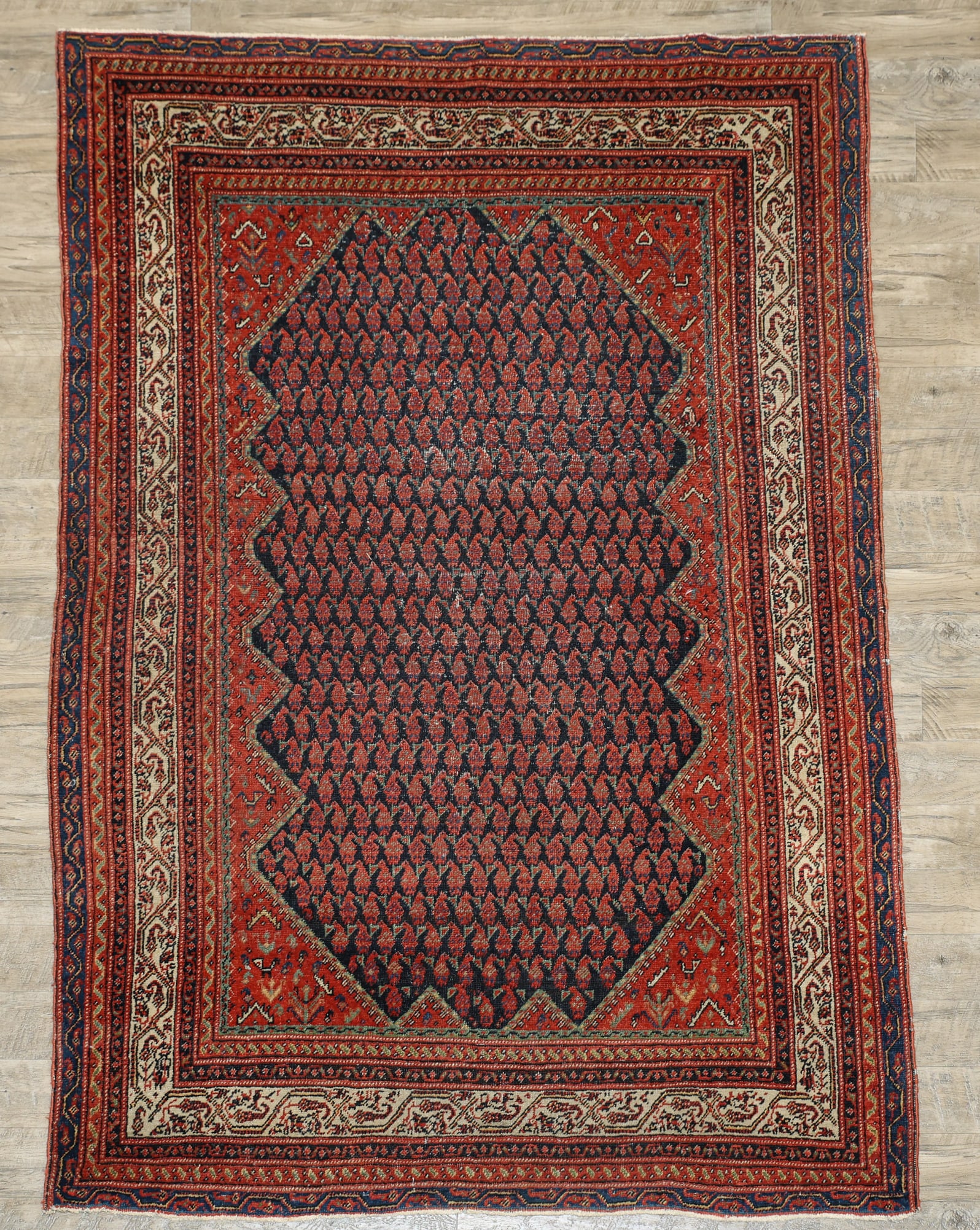 Persian Malayer Rug: Hand knotted wool pile with a jagged edge boteh motif central medallion in a navy blue field, alternating arabesque motifs in the spandrels and borders in polychrome colors of red, cream, and blue. Li