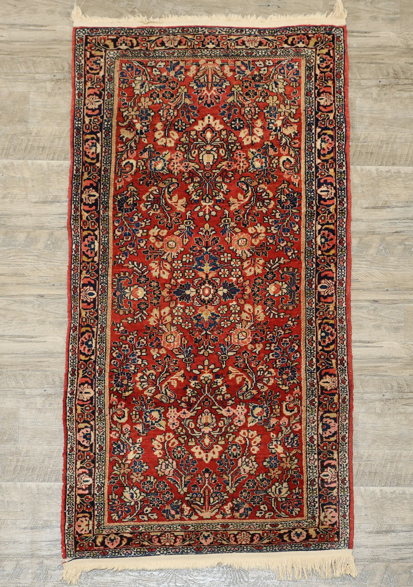 Persian Sarouk Rug: Hand knotted with all over palmette, rosette, and sprig design, straight edge palmette motifs in the main border, polychrome colors of red, navy blue, and cream. Torn area to one fringe. Early 20th c.