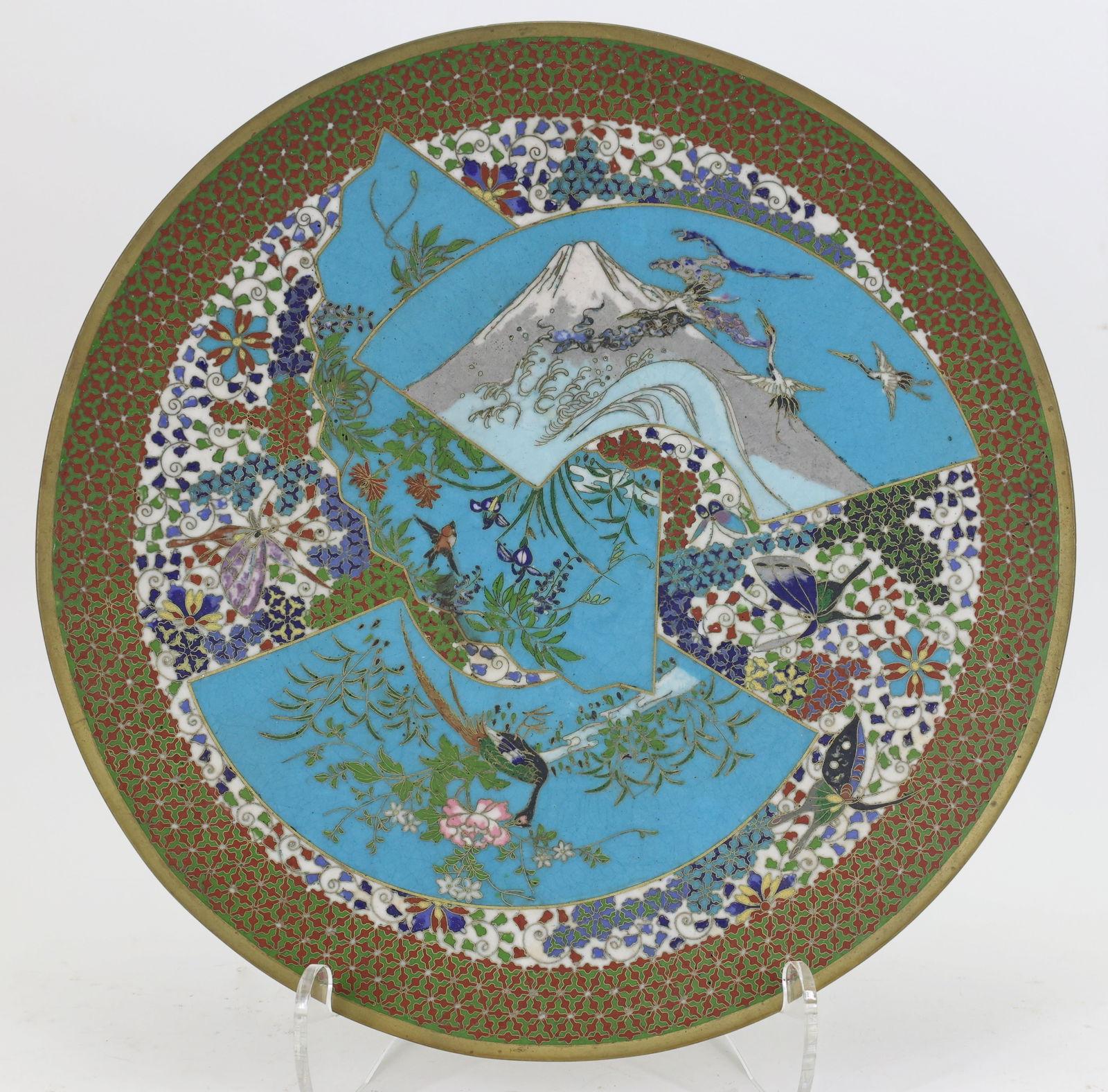 Japanese Cloisonne Charger: Meiji - Taisho era charger with fan shaped panels depicting cranes in flight with Mount Fuji in the background, a sparrow and a peacock among flowers, laid over a polychrome field of flowers and butte