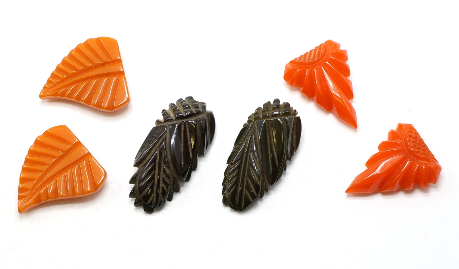 Vintage Carved Bakelite Dress Clips: Vintage Bakelite dress clips in leaf and fan motifs, including a pair in butterscotch orange, a pair in brown with carved feather forms, and a pair in orange red with sunburst designs. Largest clip me