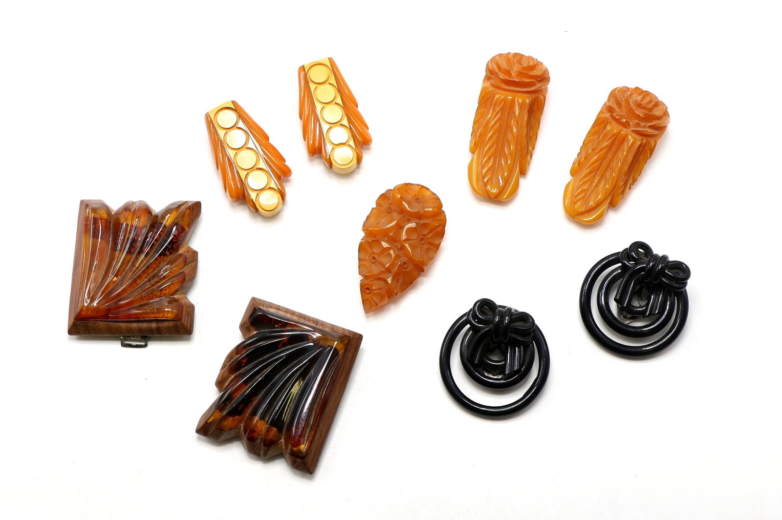 Vintage Carved Bakelite and Wood Dress Clips: Carved Bakelite dress clips in rose, dot, and leaf motifs; one carved leaf-shaped clip; one pair of molded black hoop clips with bow detail; and two laminated Bakelite and wood brooches. Largest clip