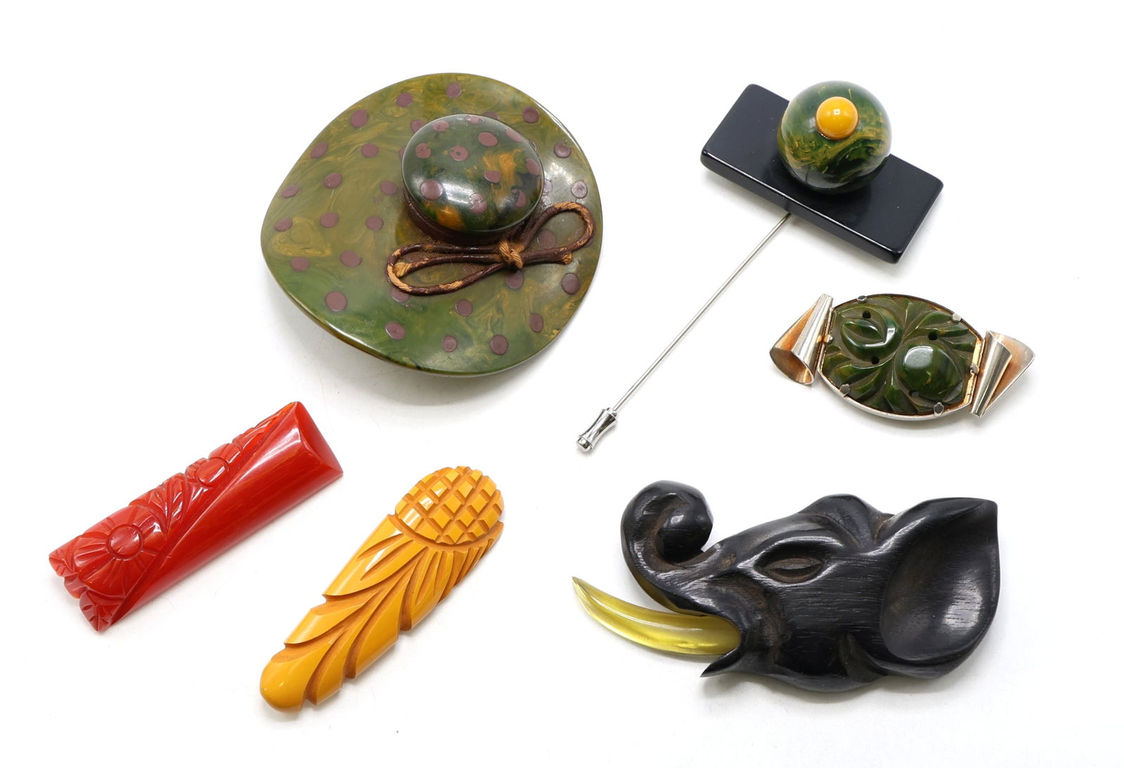 Vintage Carved Bakelite and Wood Pins: Carved green and maroon hat brooch with molded dome, a black rectangular stickpin with a green swirl dome and yellow cabochon, an oval carved green swirl brooch, a red floral carved brooch, a buttersc