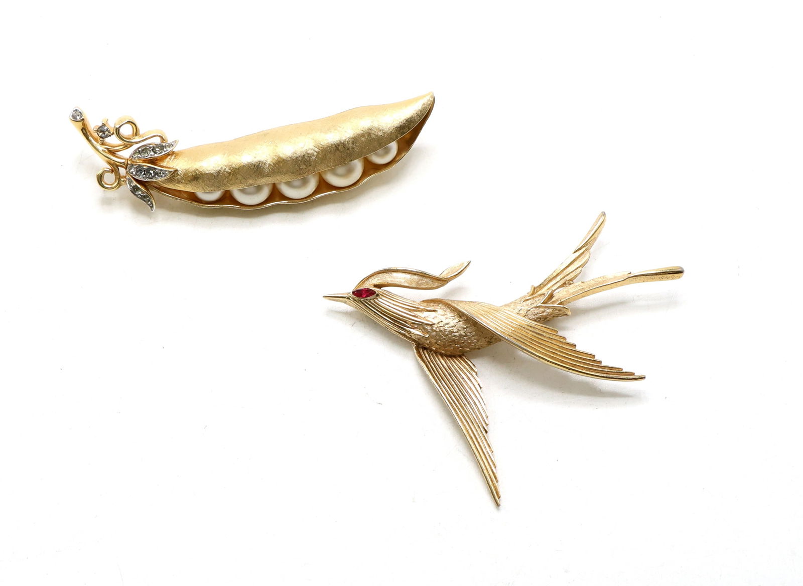 Trifari Bird and Peapod Brooches: Trifari gold-tone peapod brooch featuring faux pearls and rhinestone-accented leaves. Friend gold-tone bird brooch with textured details and red rhinestone eye. Largest pin measures 2.75”w