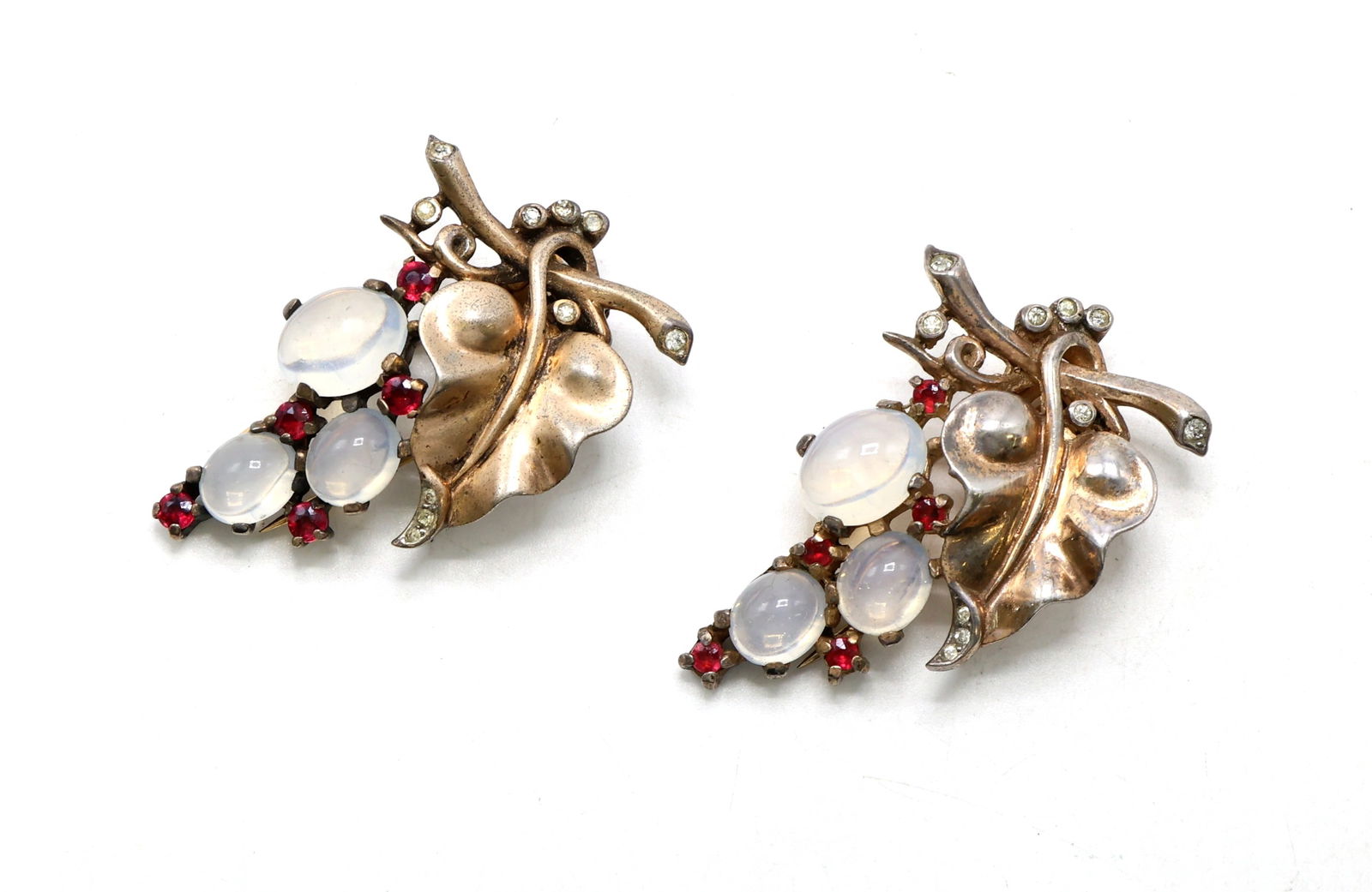 Trifari Clips with Rhinestones and Moonstone Accents: Trifari dress clips featuring leaf motifs adorned with rhinestones and moonstone-like cabochons. Reverse marked with Trifari crown logo. Both measure 1.75”h